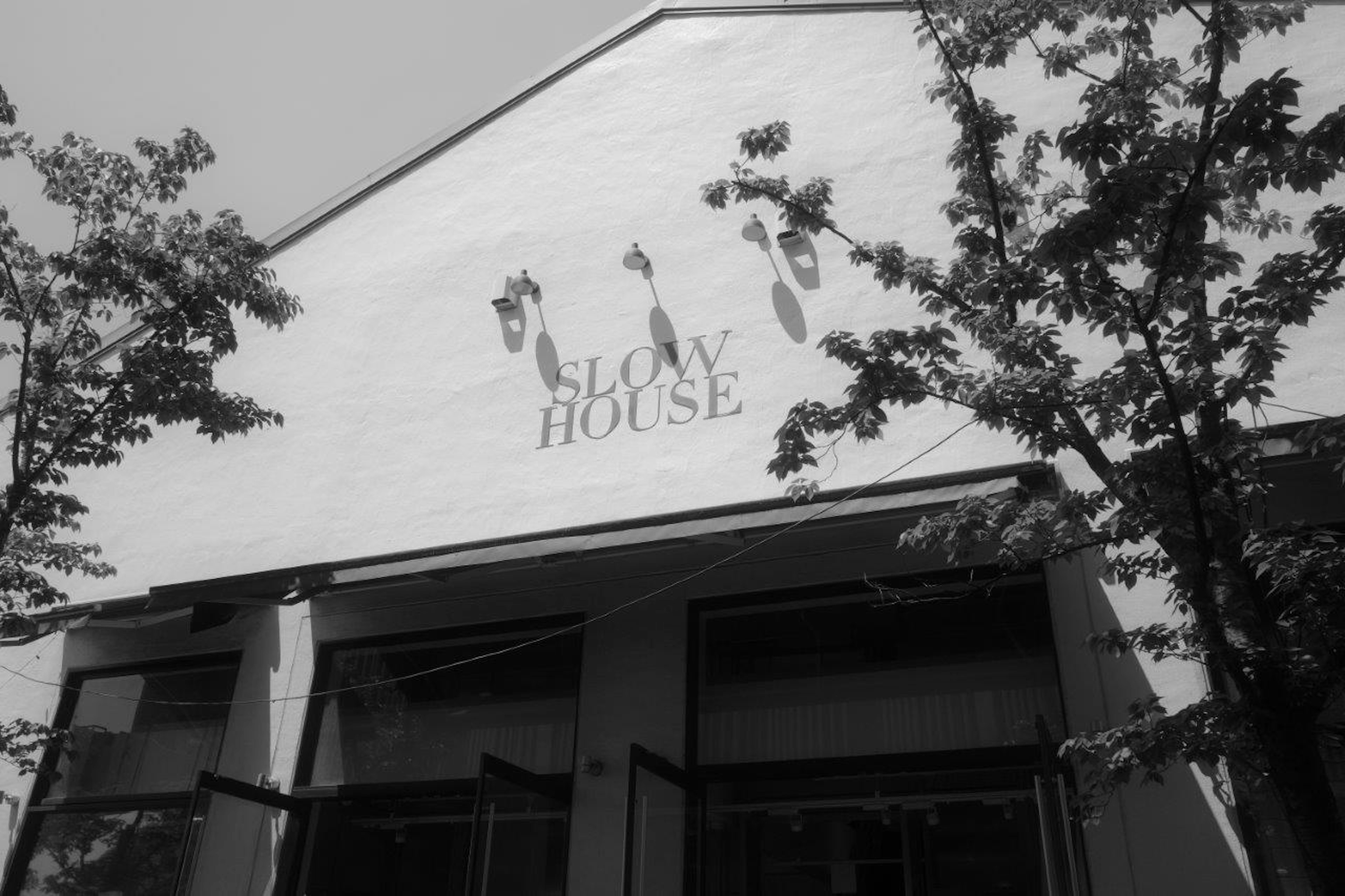 ภายนอกอาคารที่มีโลโก้ Slow House ล้อมรอบด้วยต้นไม้