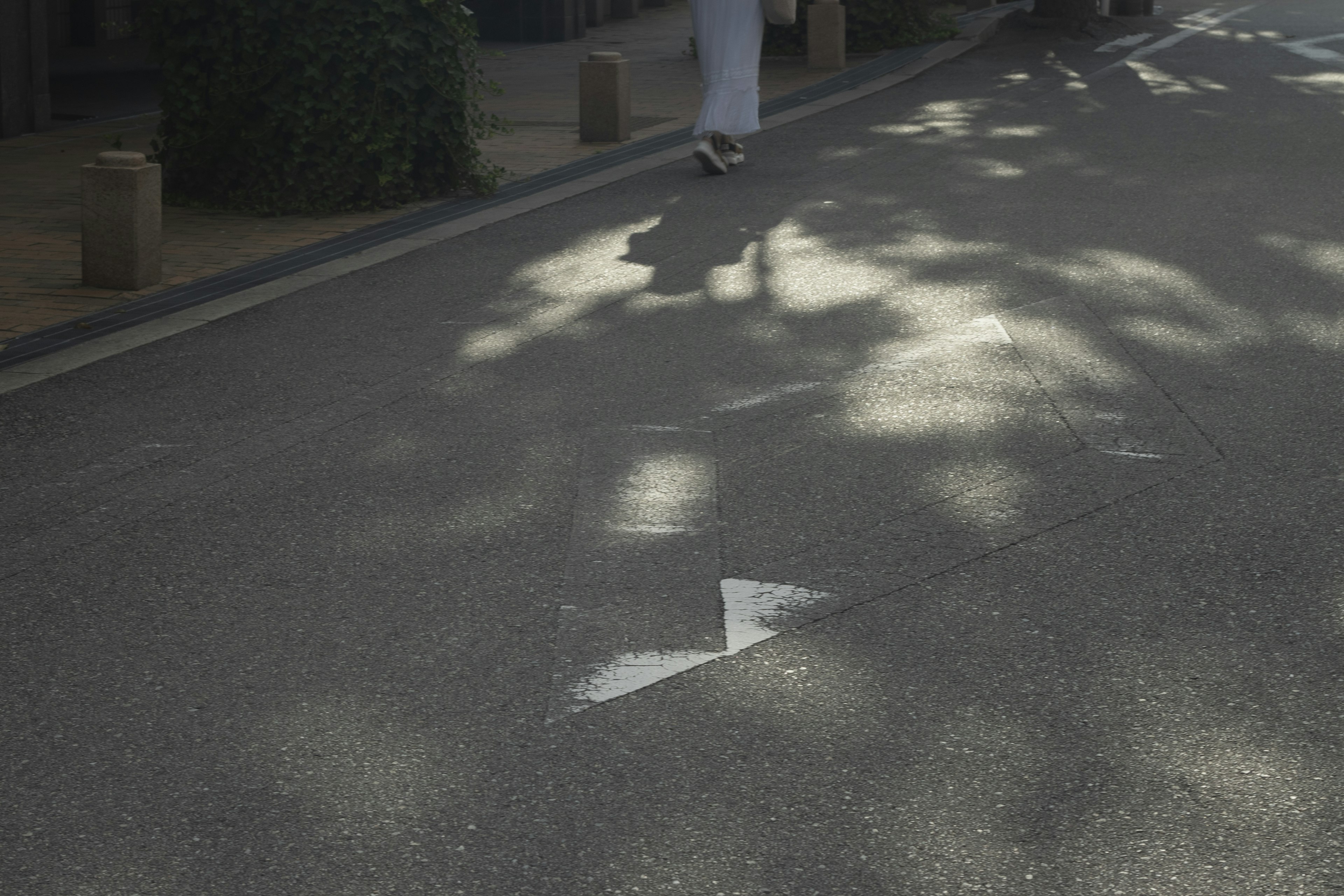 Flecha blanca en carretera de asfalto con sombras y persona caminando