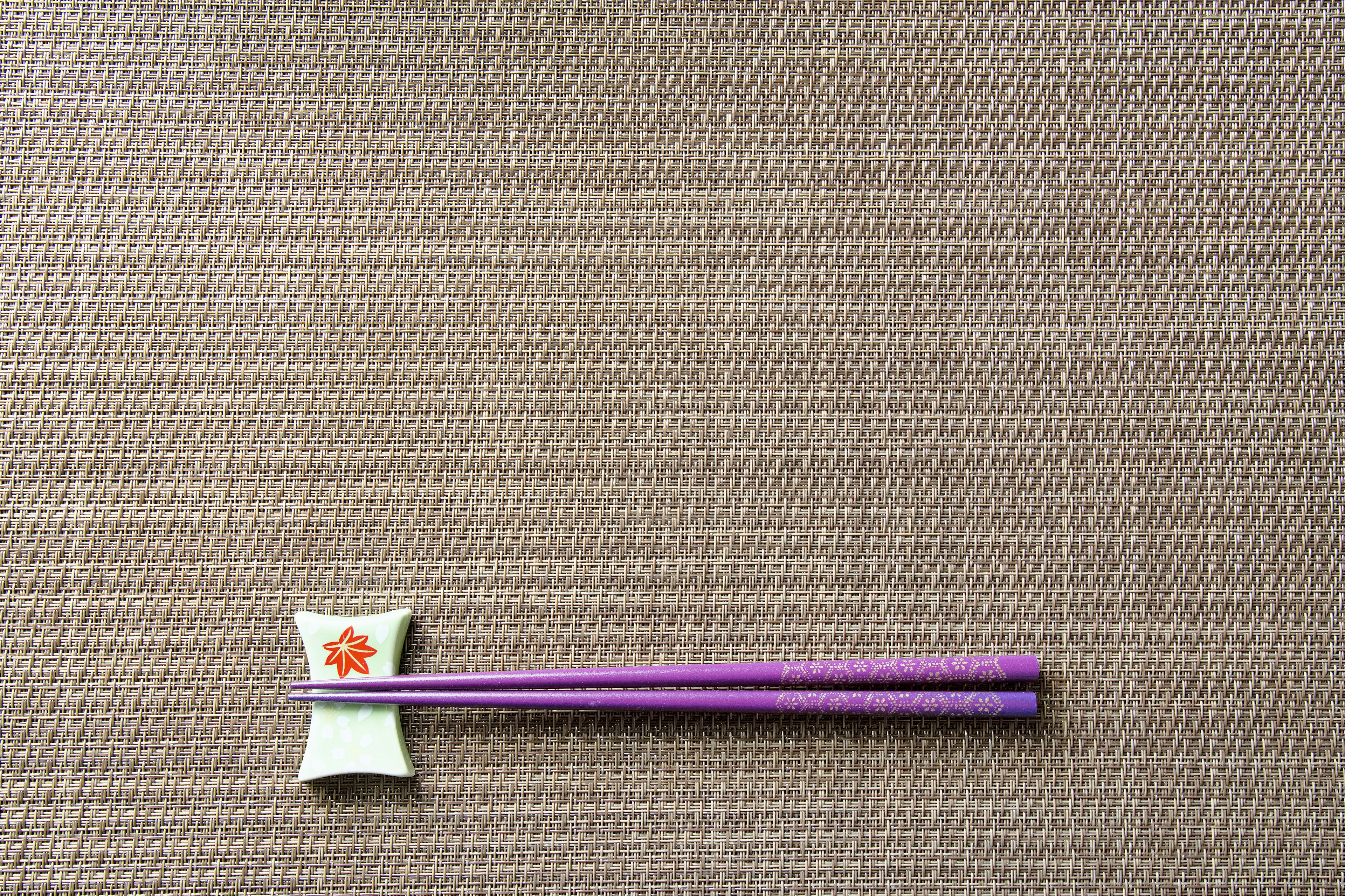 Purple chopsticks placed beside a flower-patterned chopstick rest on a textured table