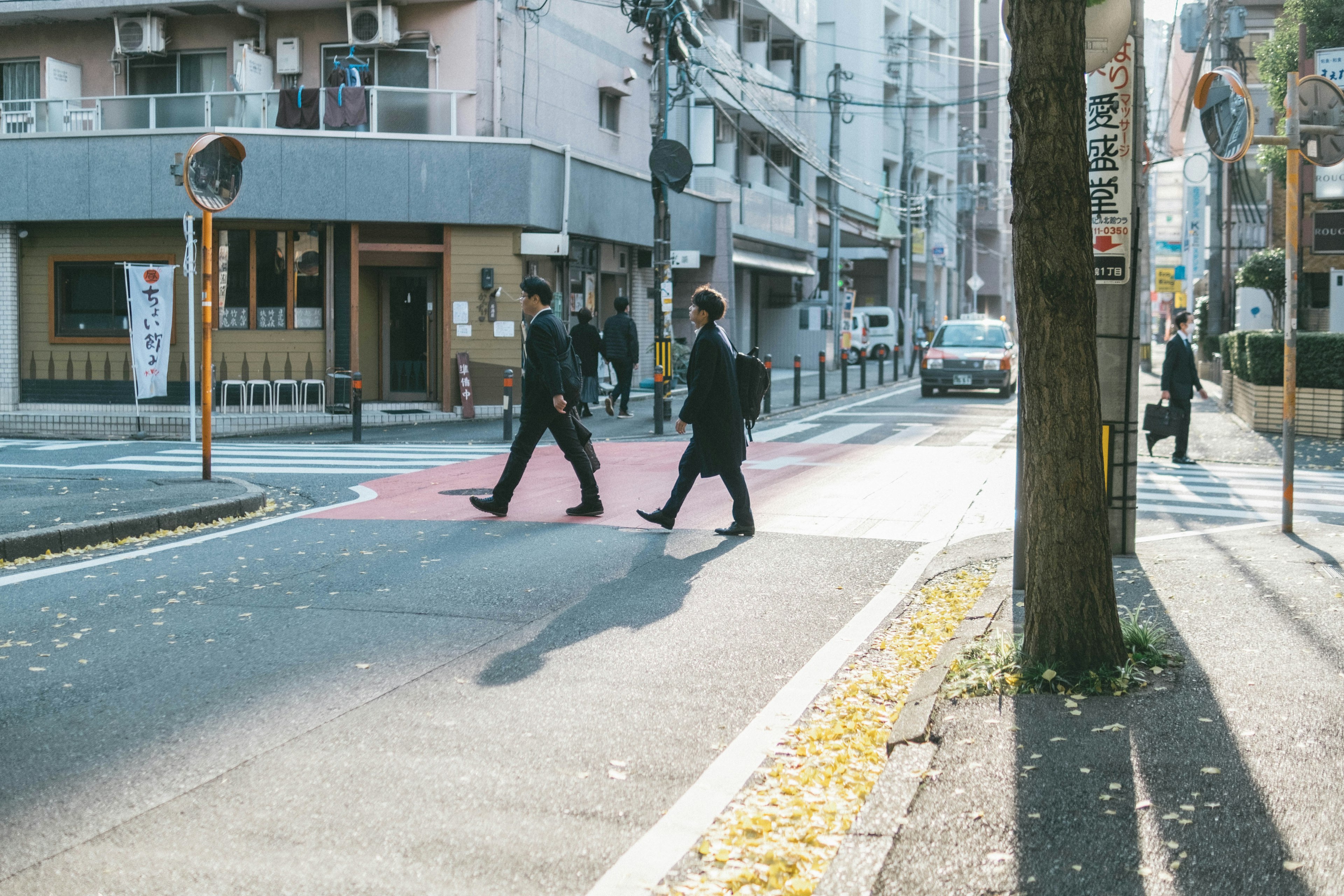 街を横断するスーツ姿の男性たちと秋の風景