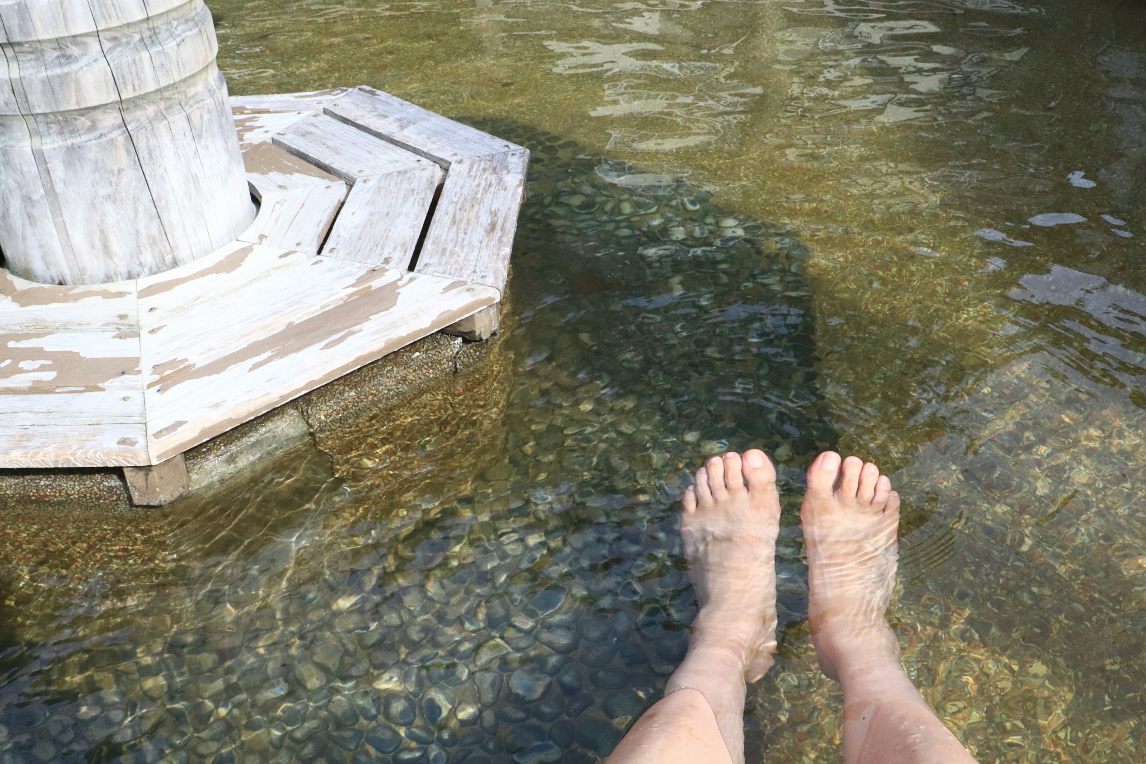 Feet submerged in clear water near a wooden structure