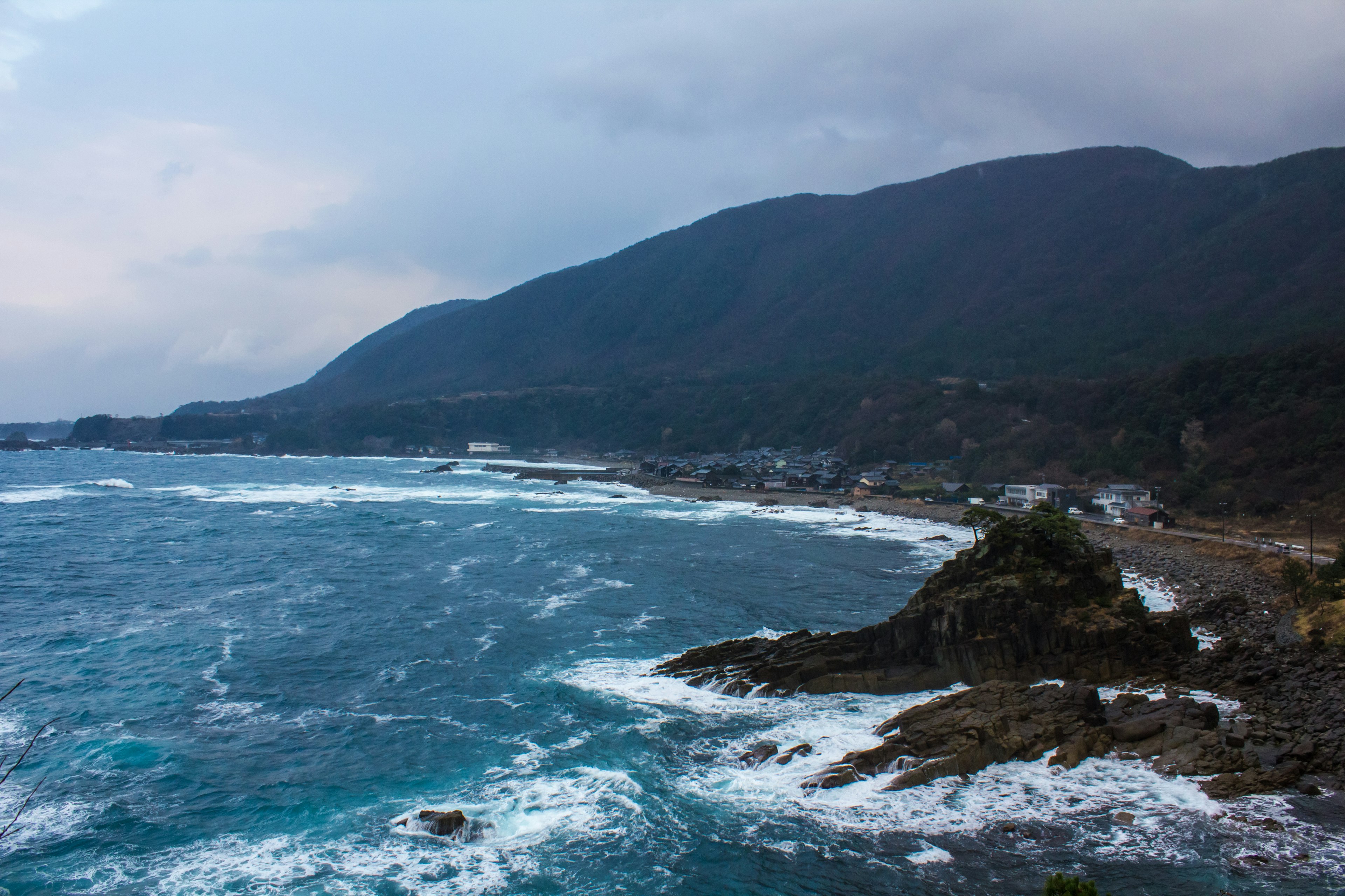 Coastal landscape with mountains in the background waves crashing against rocks overcast sky