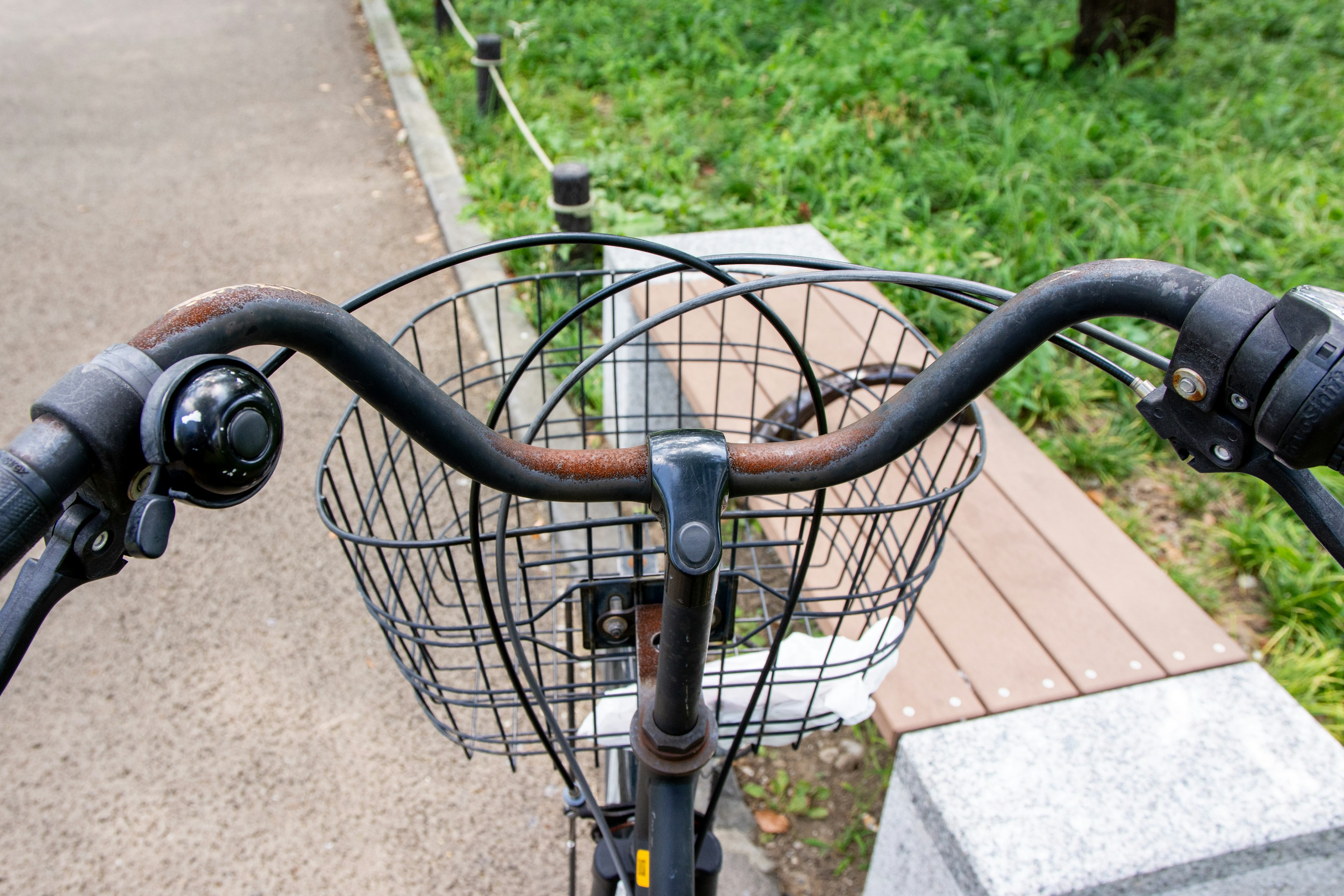 View from above a bicycle handlebars with a wire basket green grass in the background