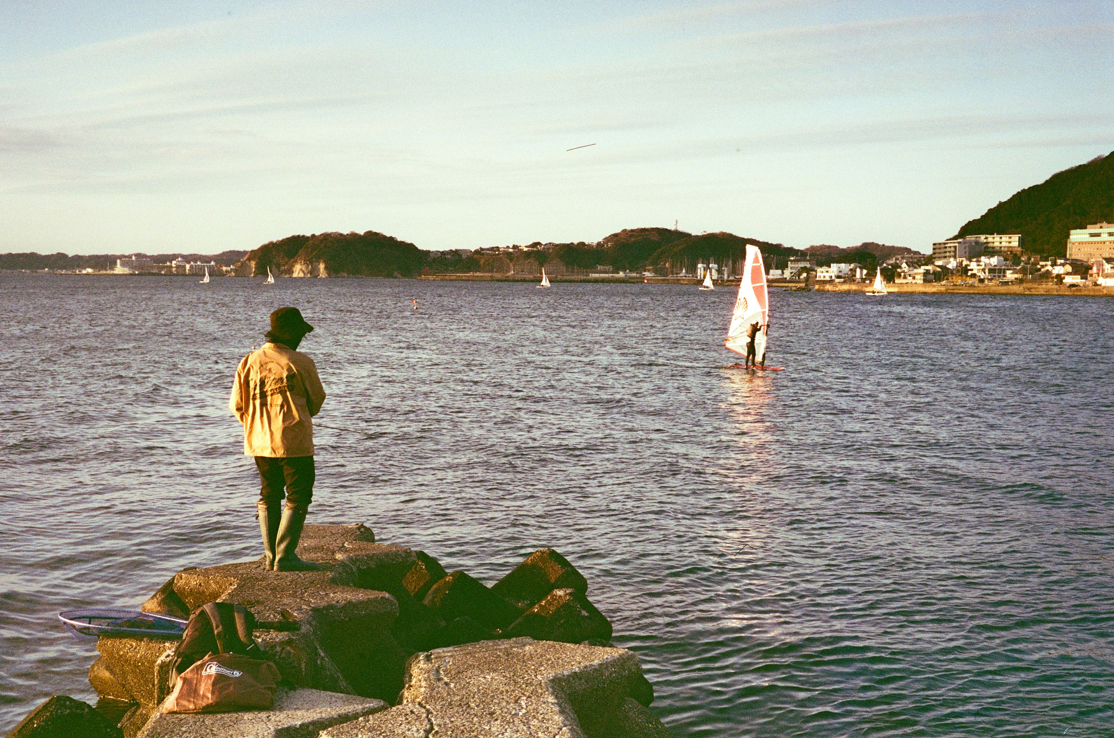 Person standing on rocky shore with sailboat in the background