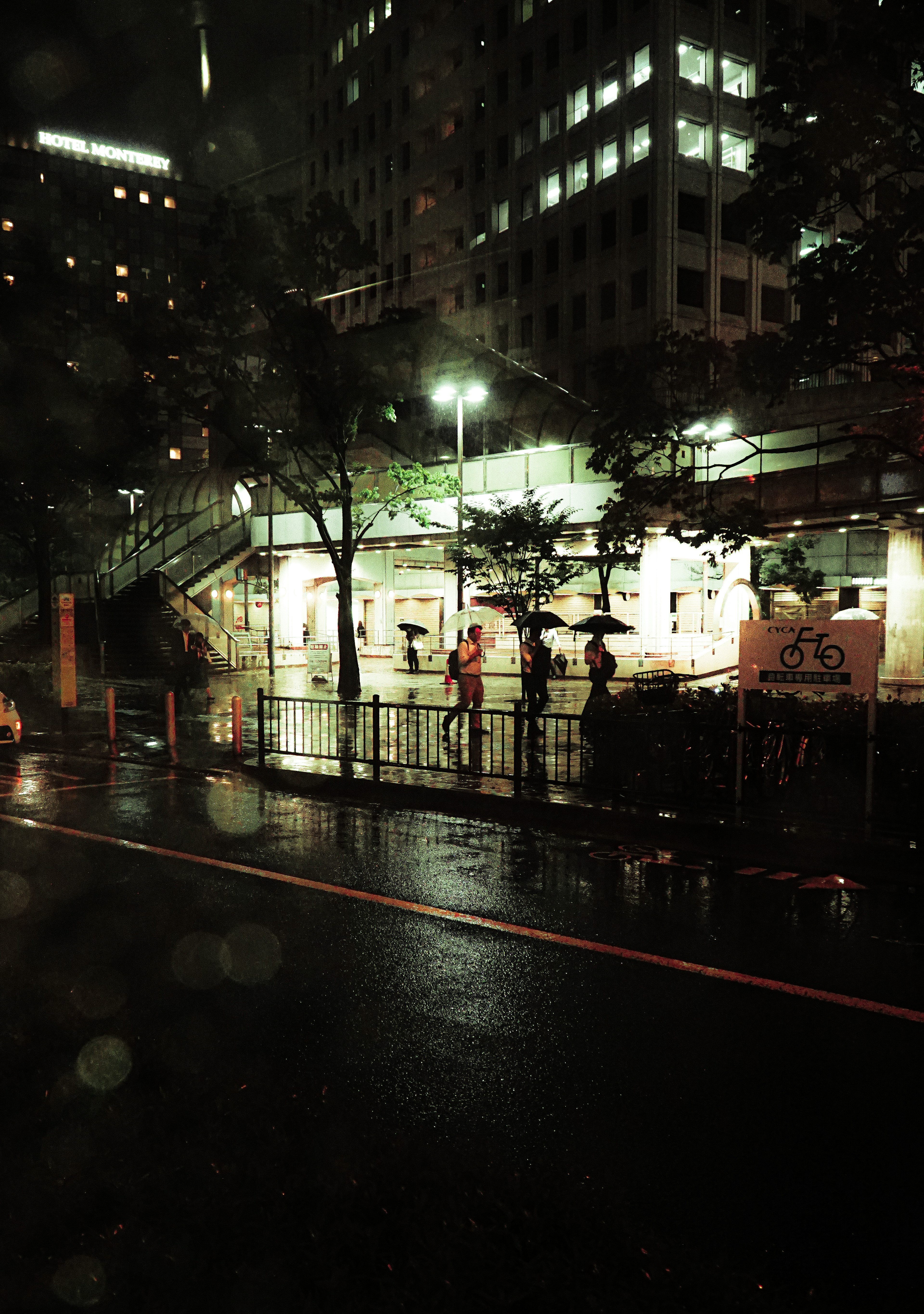 Night city scene with people holding umbrellas and rain-soaked street