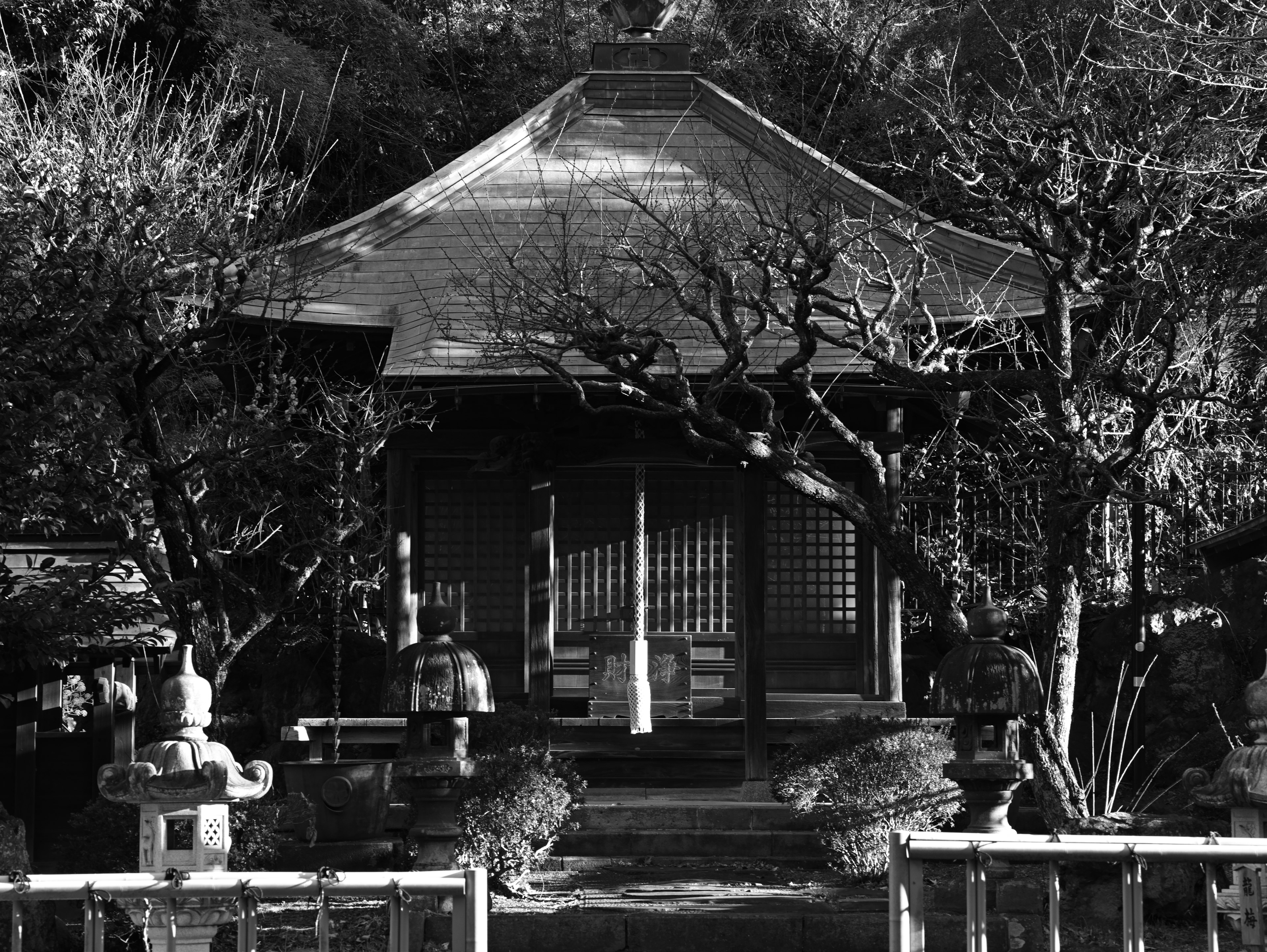 Black and white image of a temple with surrounding trees and stone statues