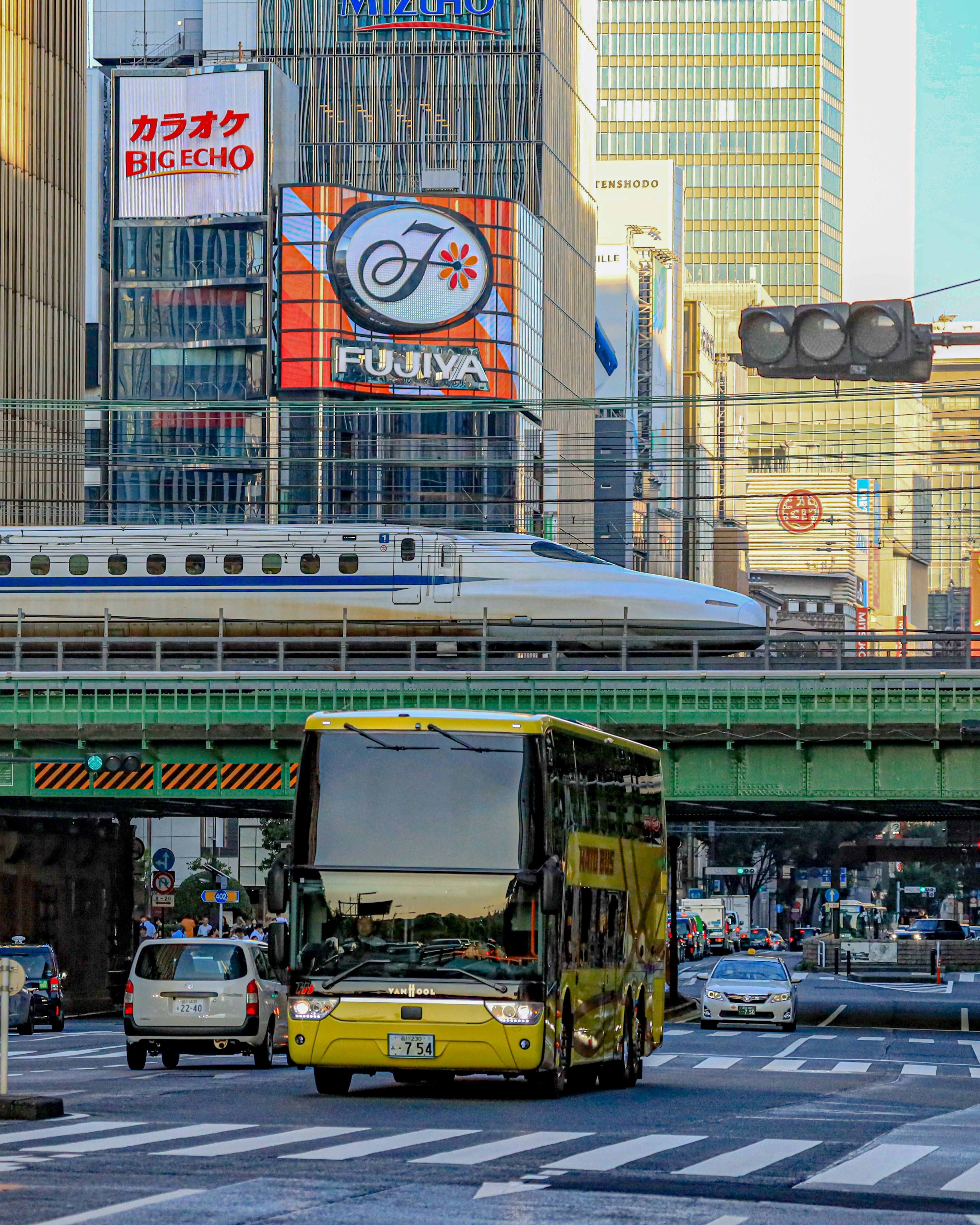 Un autobús de dos pisos amarillo en una escena urbana bulliciosa con un tren Shinkansen