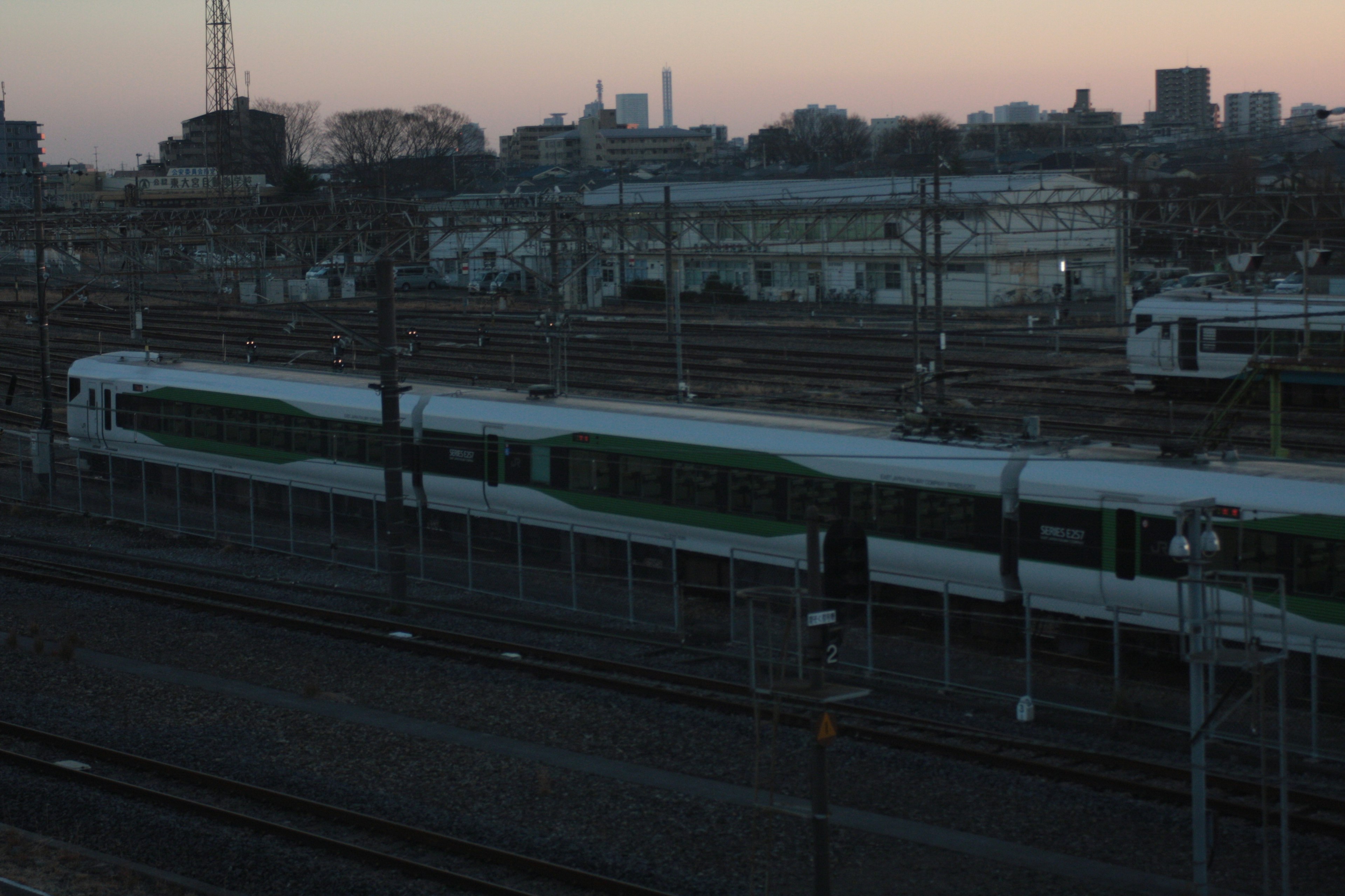 Escena ferroviaria al atardecer con tren verde y vías