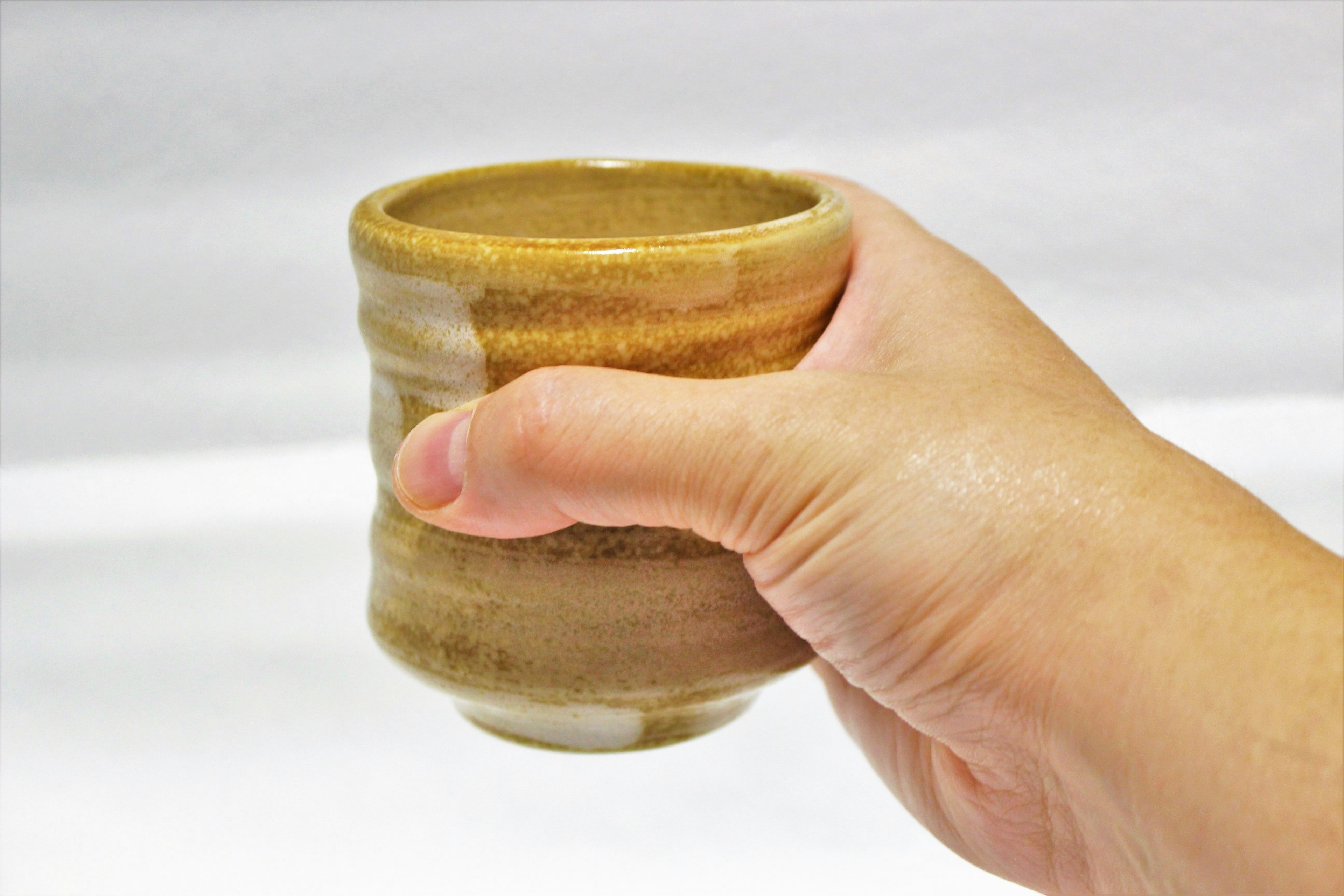 Hand holding a ceramic cup with cream and brown striped pattern