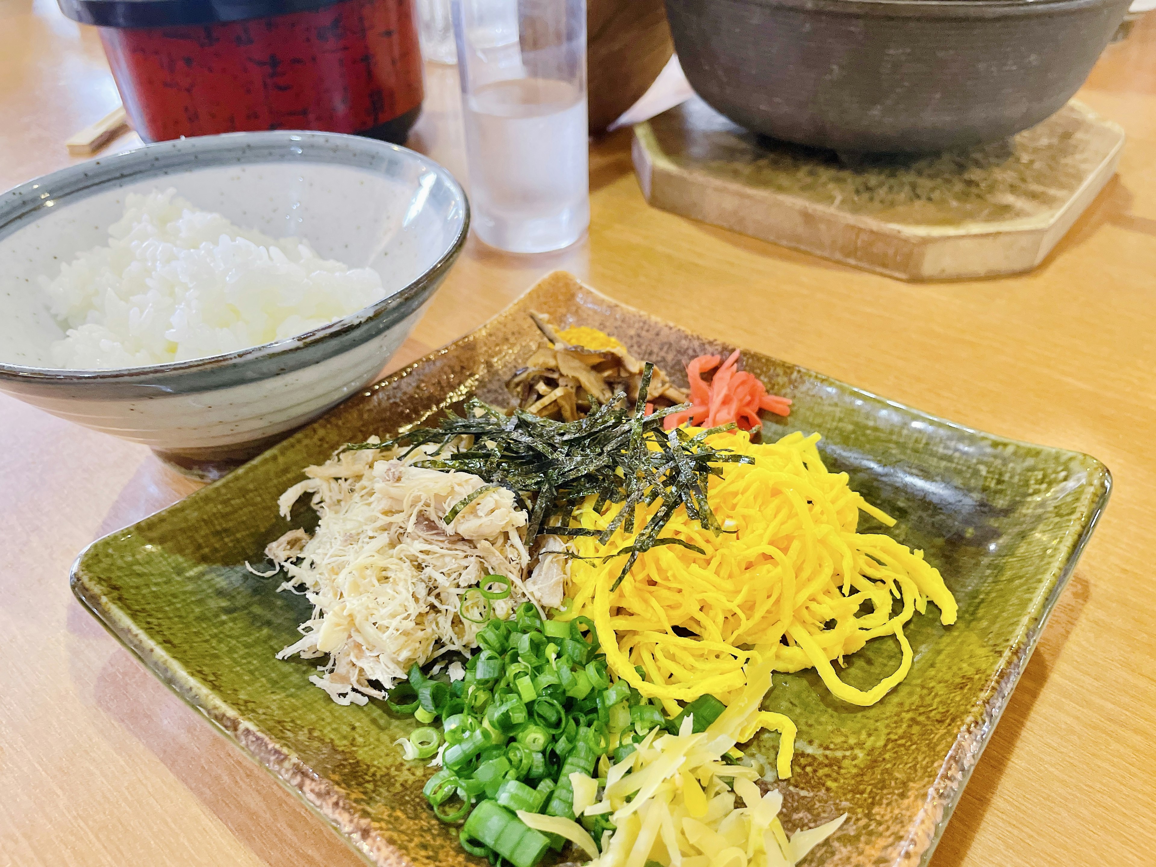 Une assiette avec des ingrédients colorés, y compris du poulet effiloché, un œuf jaune et des oignons verts à côté d'un bol de riz blanc