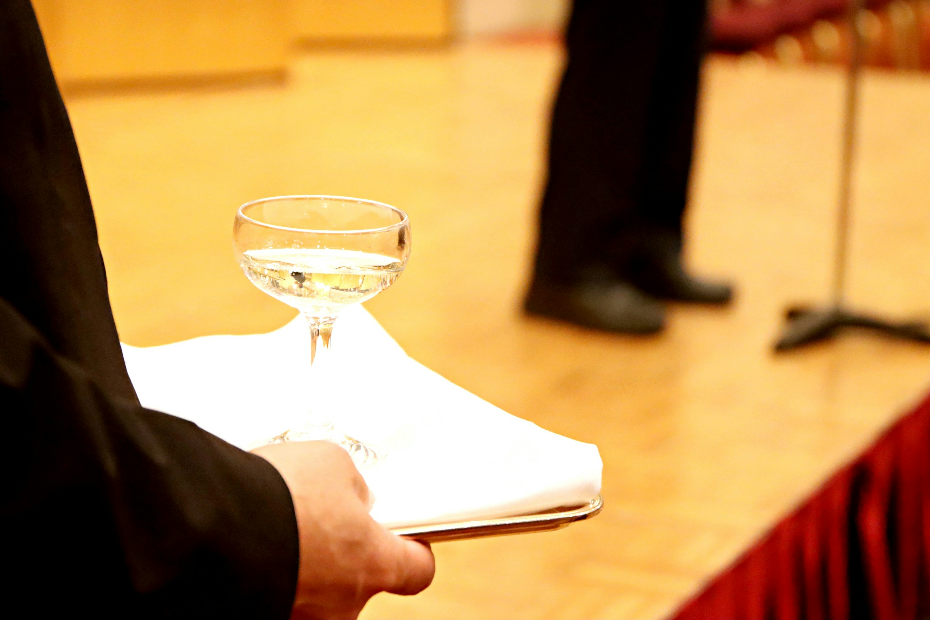 Immagine parziale di una persona che tiene un bicchiere di cocktail con uno sfondo sfocato di palco