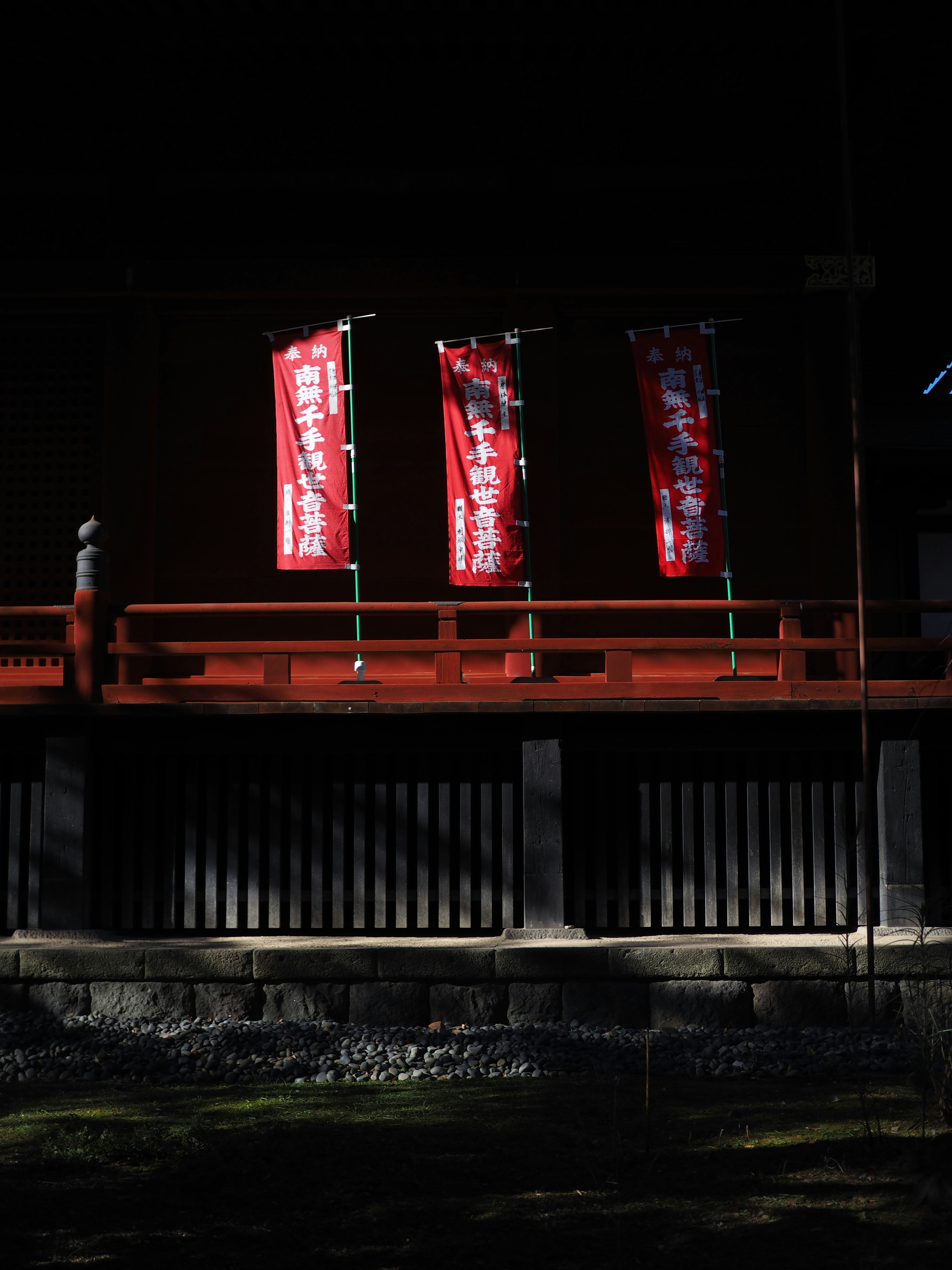 暗い背景に赤い旗が並ぶ神社の風景