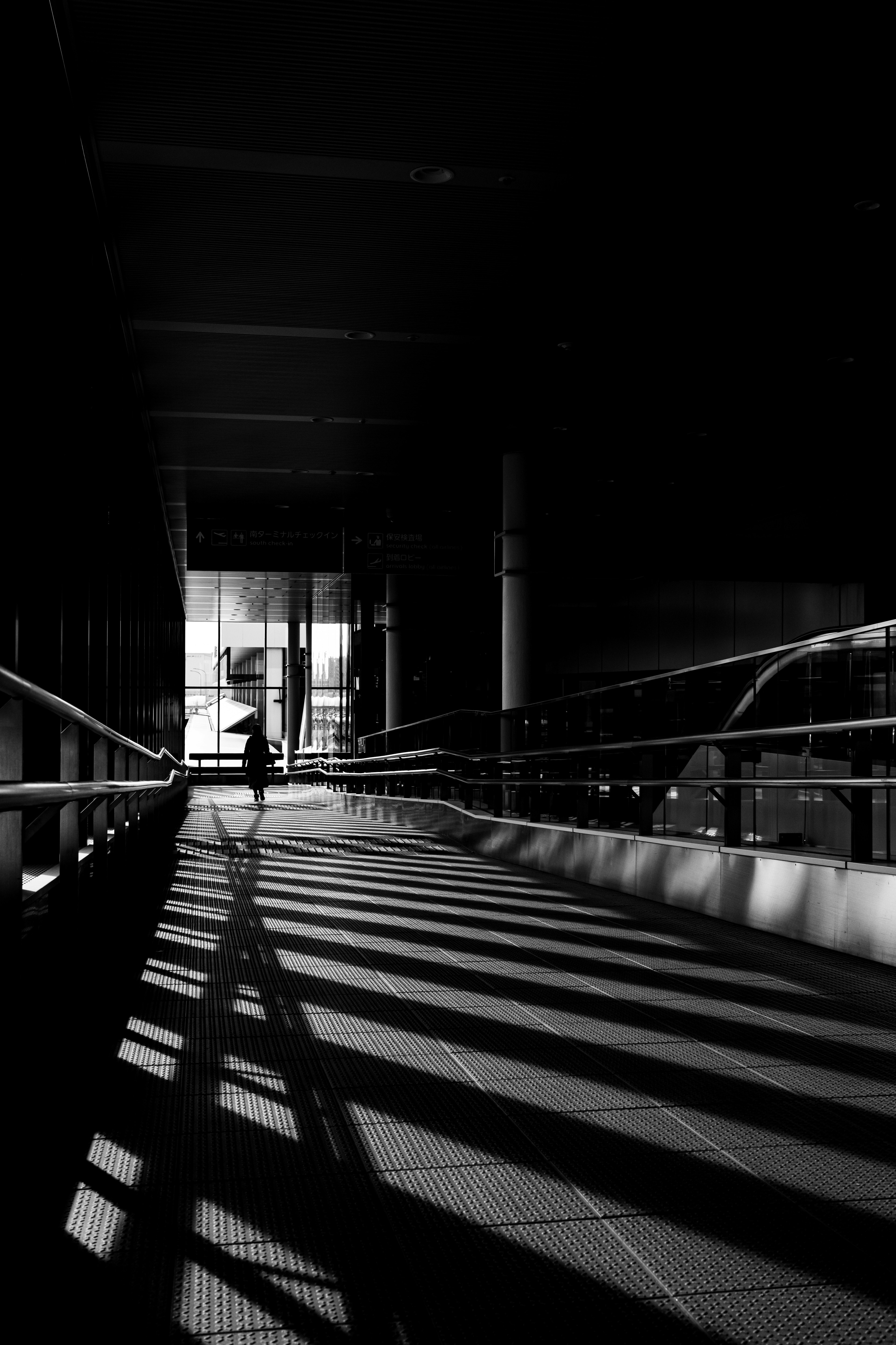 Photo en noir et blanc d'une silhouette marchant dans un couloir sombre avec de longues ombres