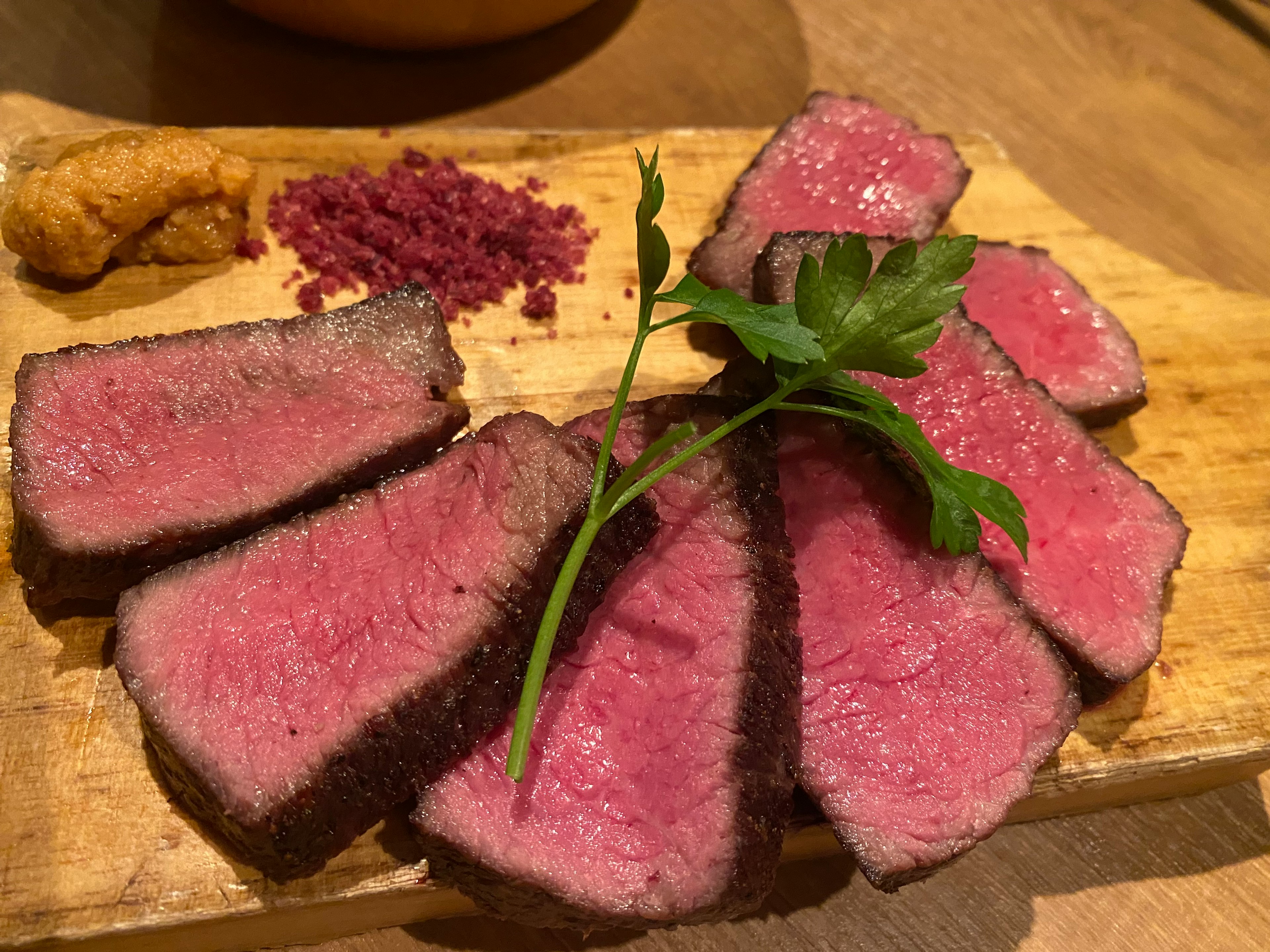 Deliciously sliced red meat on a wooden board with parsley and spice topping