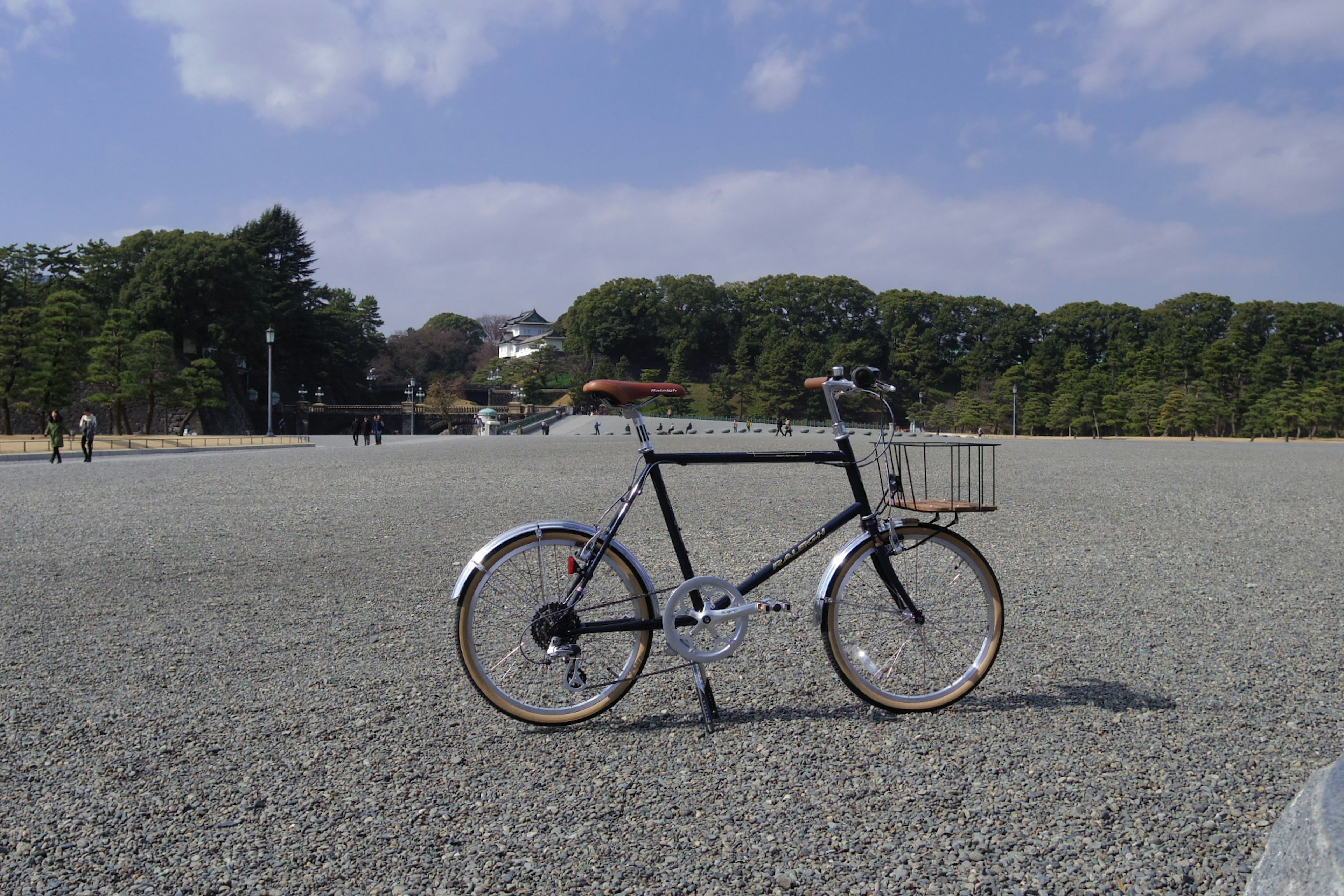 Una bicicleta negra y blanca sobre grava gris con árboles verdes y cielo azul de fondo