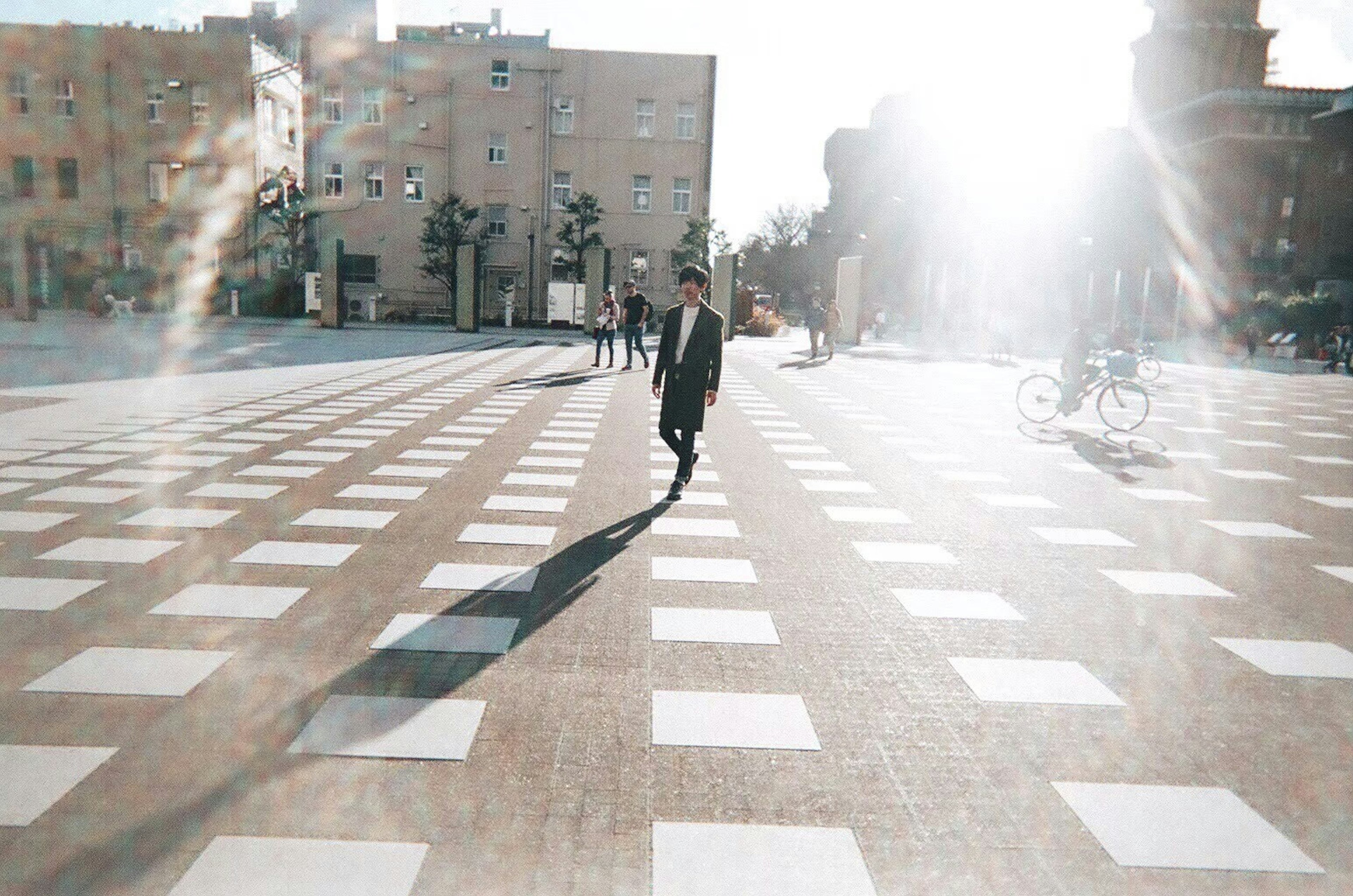 A person walking in bright sunlight on a patterned square with white tiles