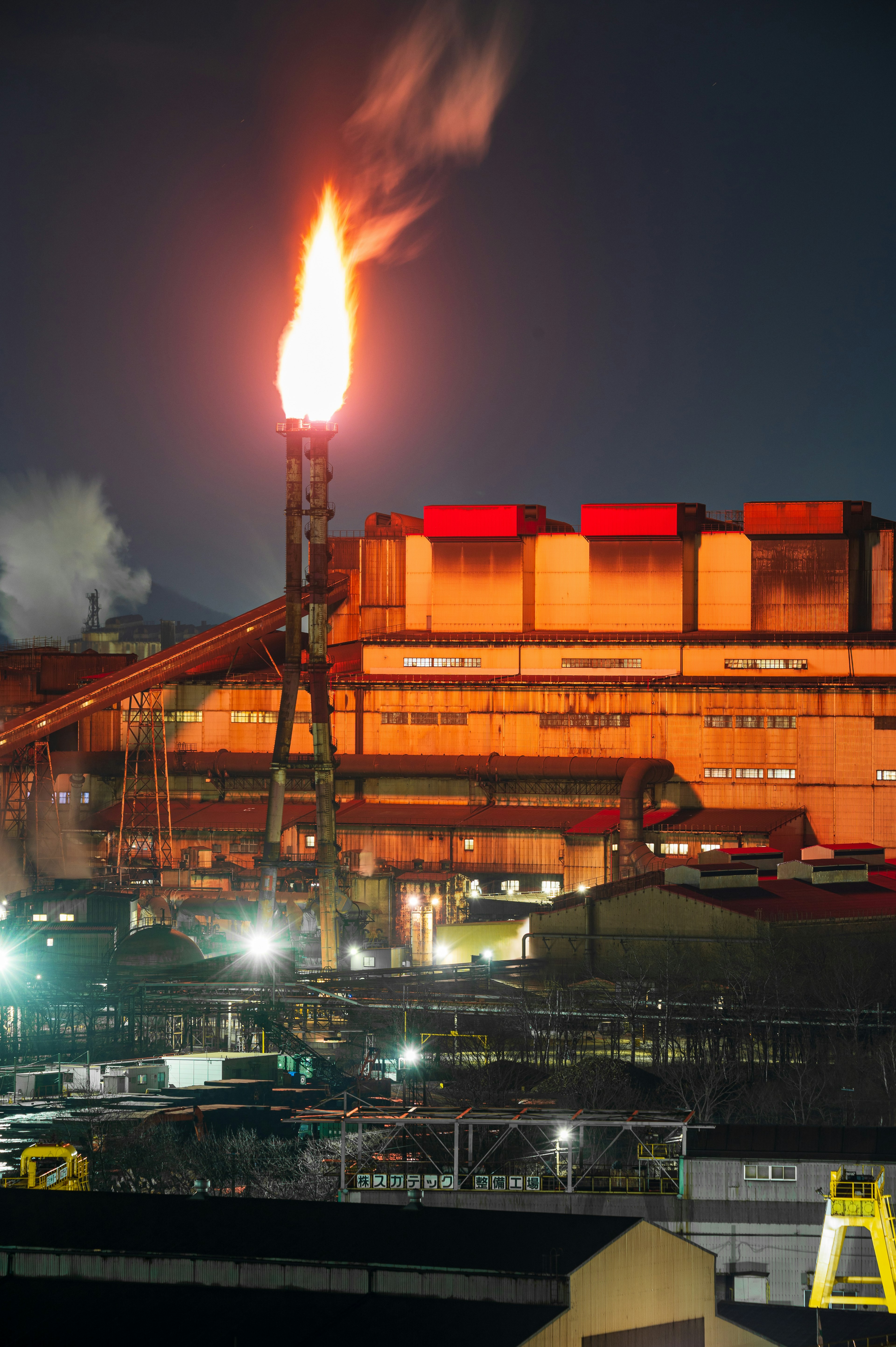 Vue nocturne d'une usine industrielle avec une flamme et de la fumée