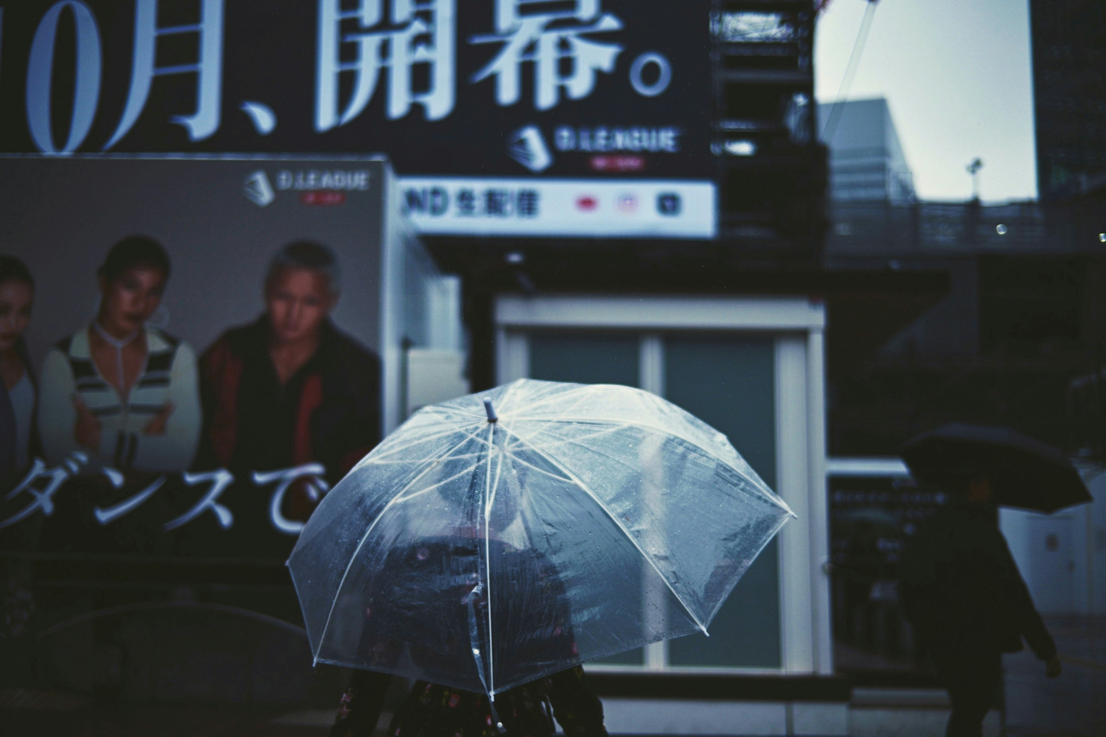 Person walking with a transparent umbrella in the city with visible advertisements