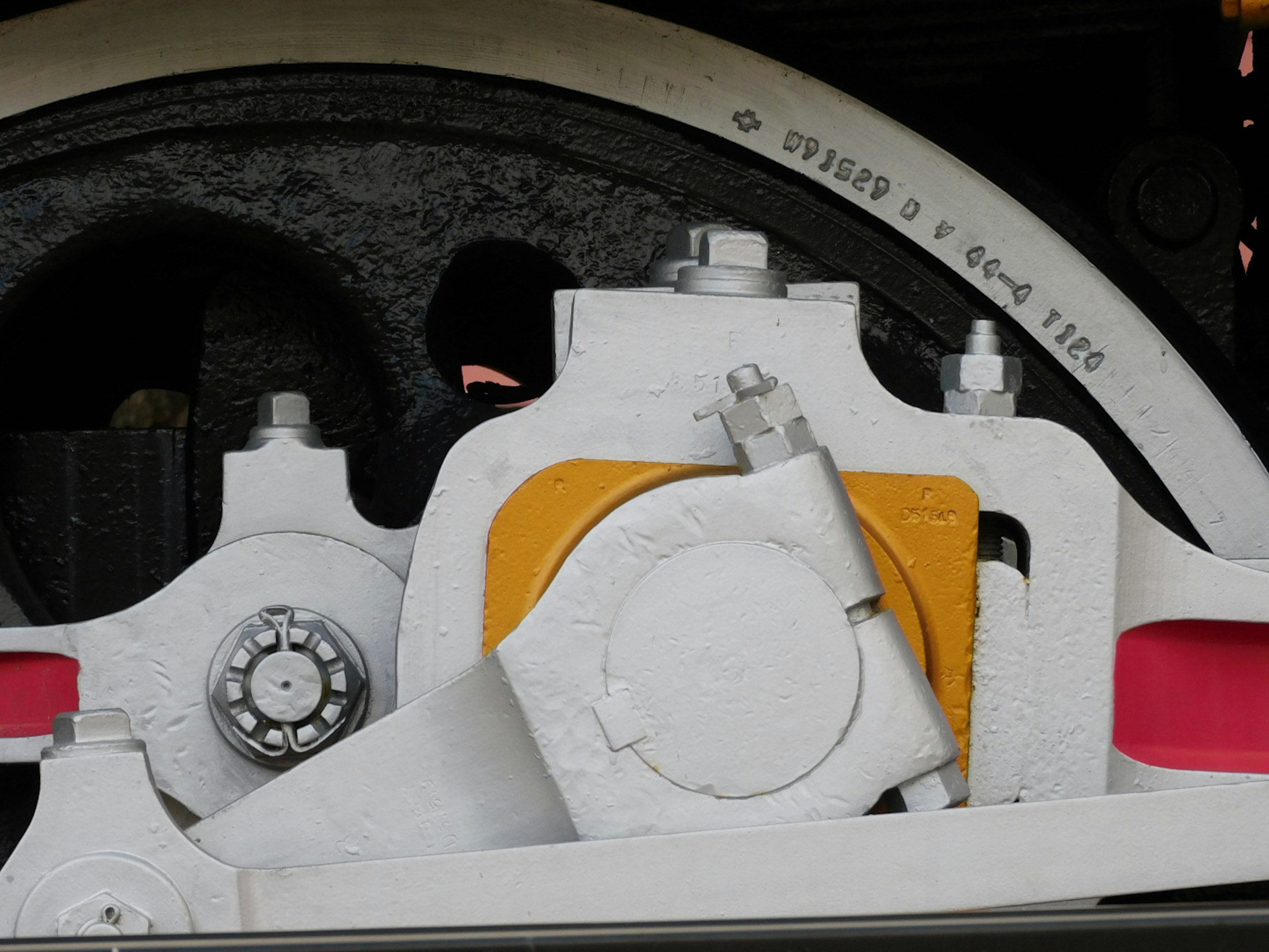 Close-up of a steam locomotive engine component featuring white and yellow metal parts with black wheel details