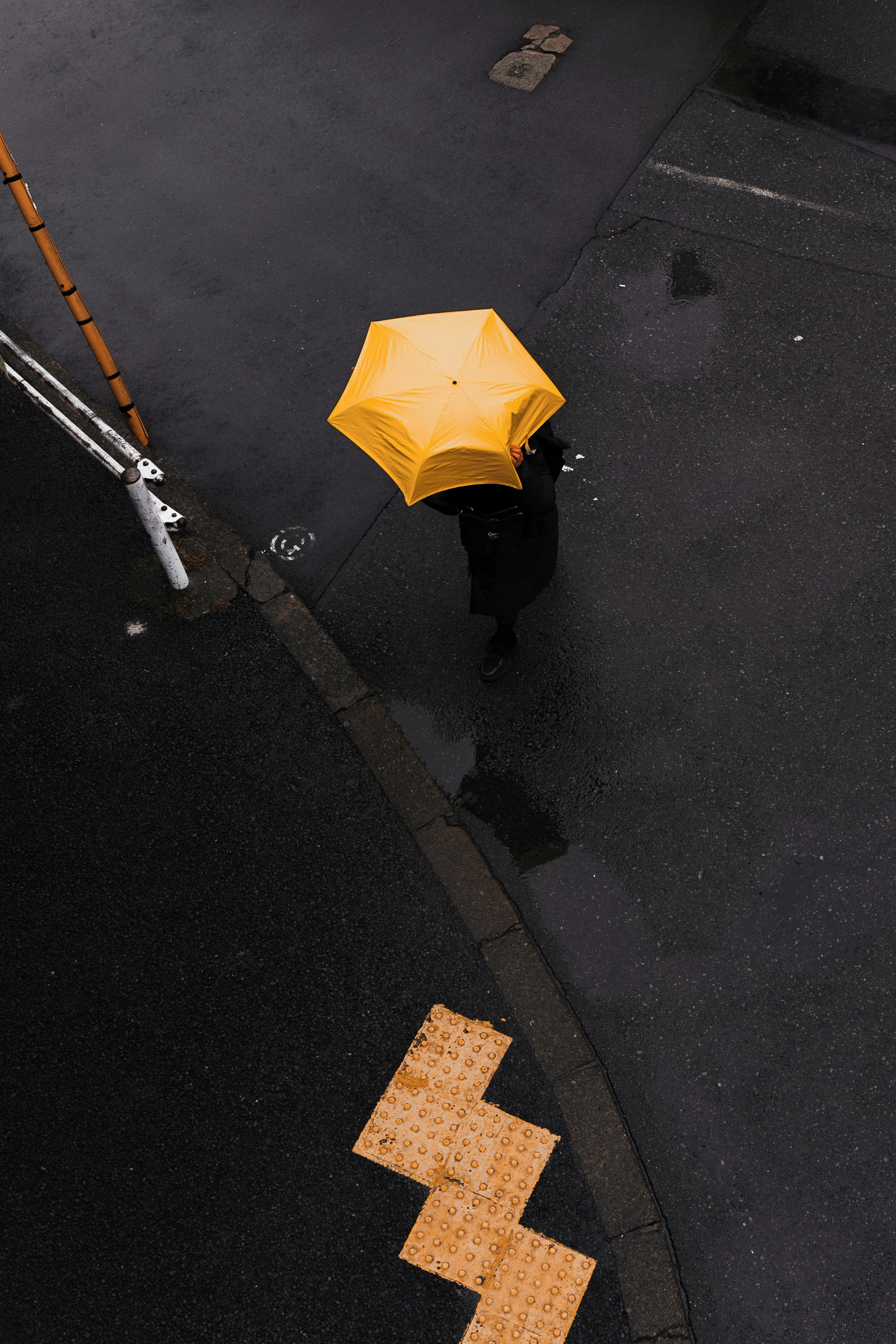 A person walking on a wet road holding a yellow umbrella