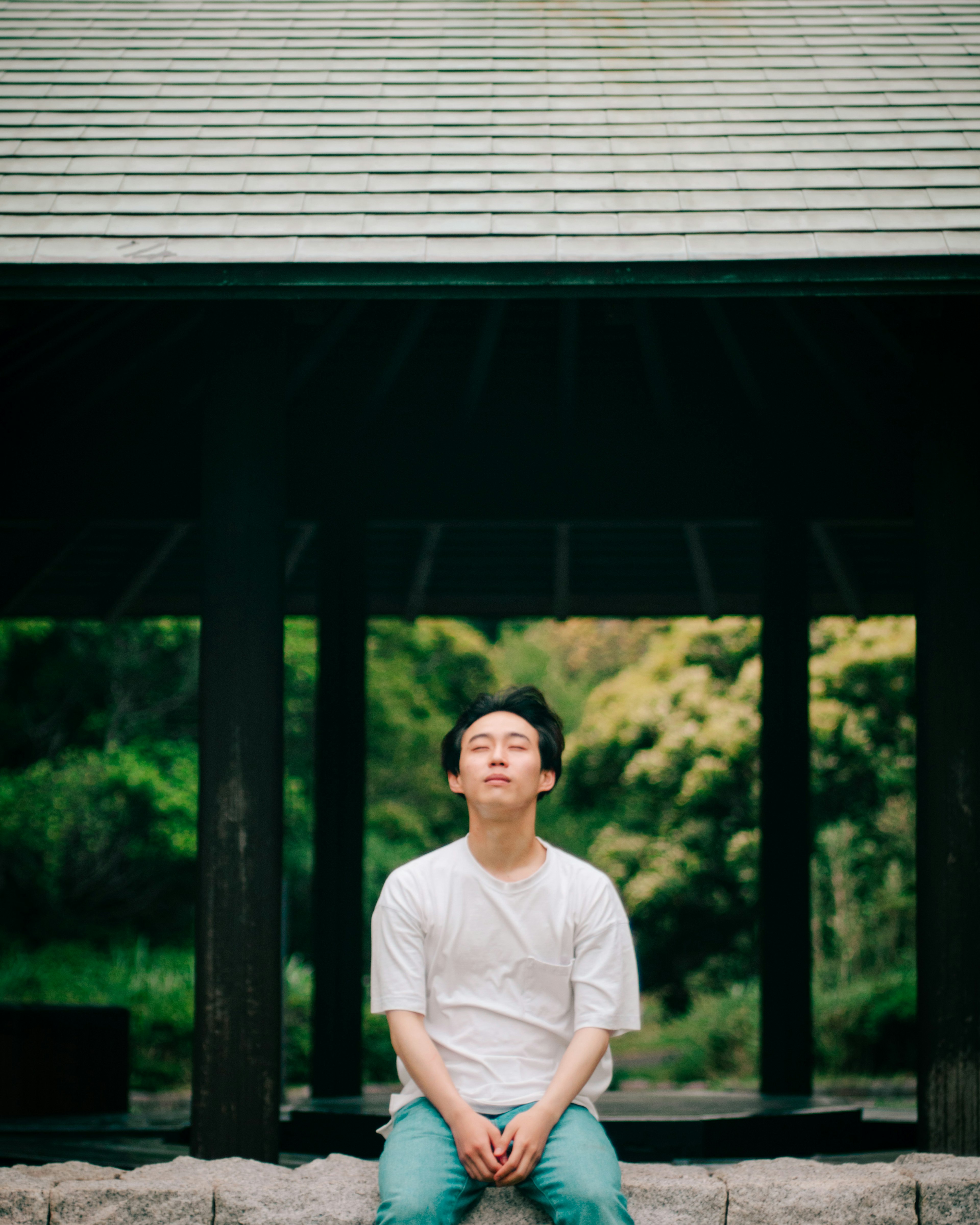 A man in a white shirt and blue pants sitting in a green background