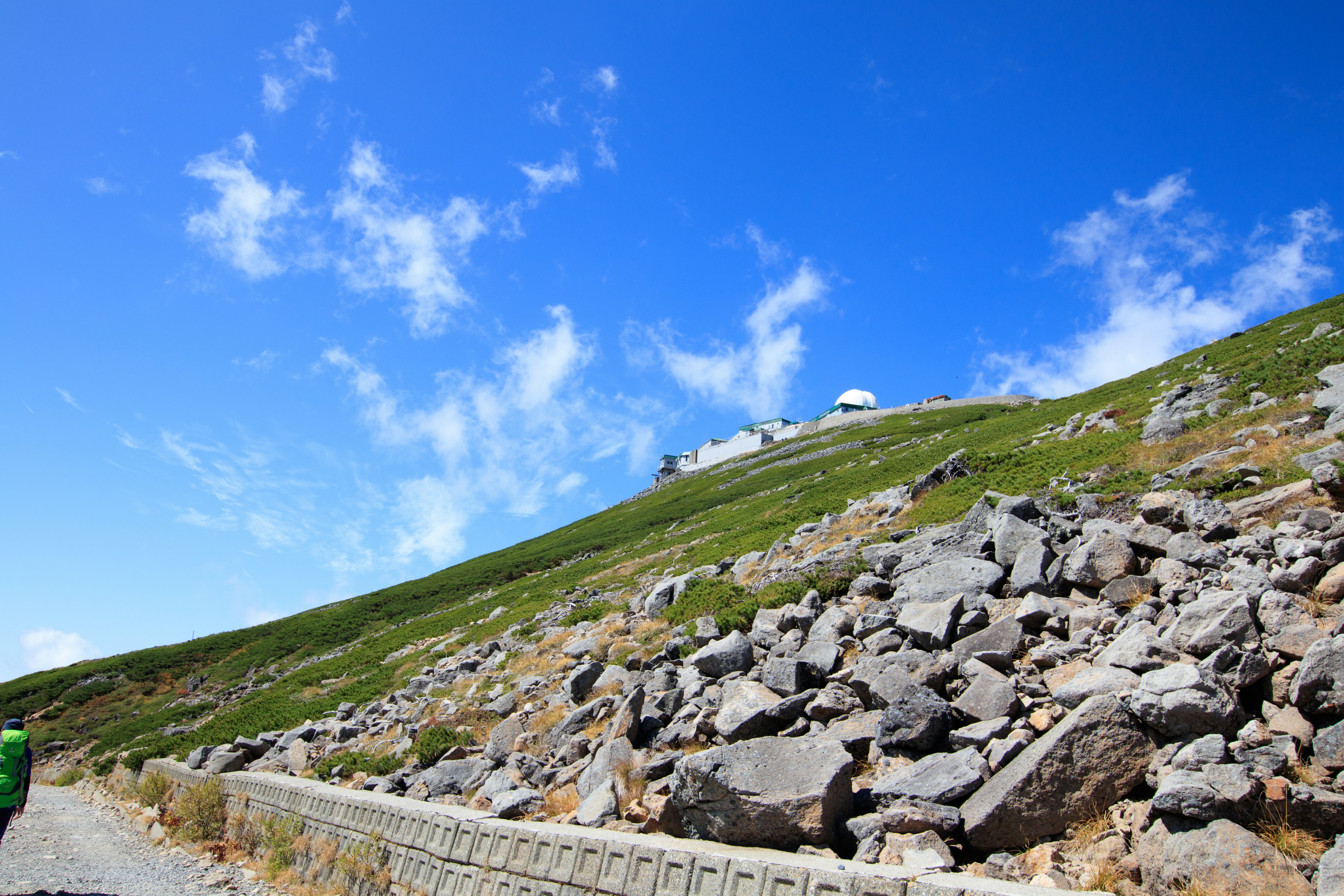 青い空と緑の山が広がる風景 石が散らばった斜面と道路が見える