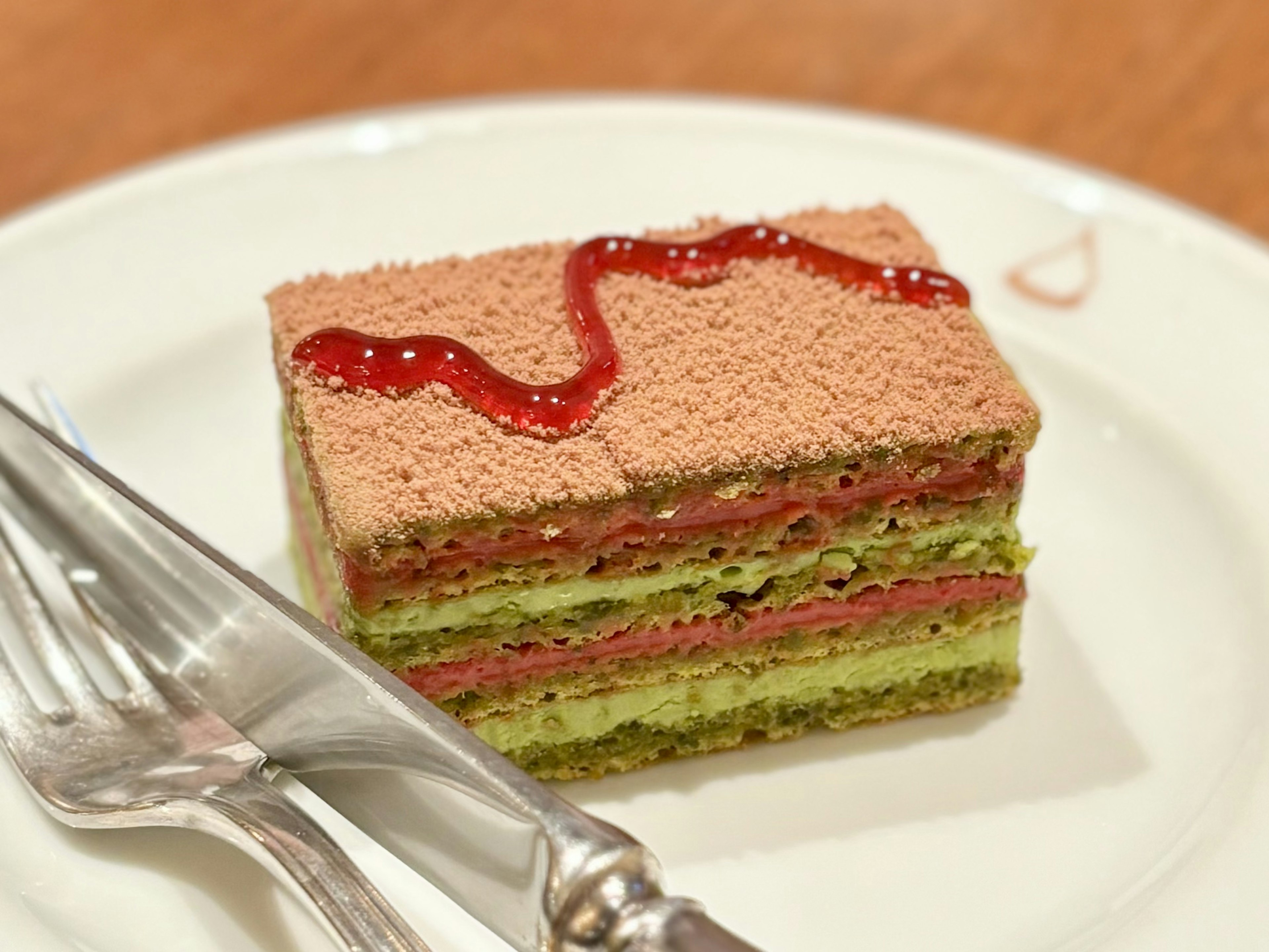 Rebanada de pastel en capas con capas verdes y rojas cubierta con salsa roja