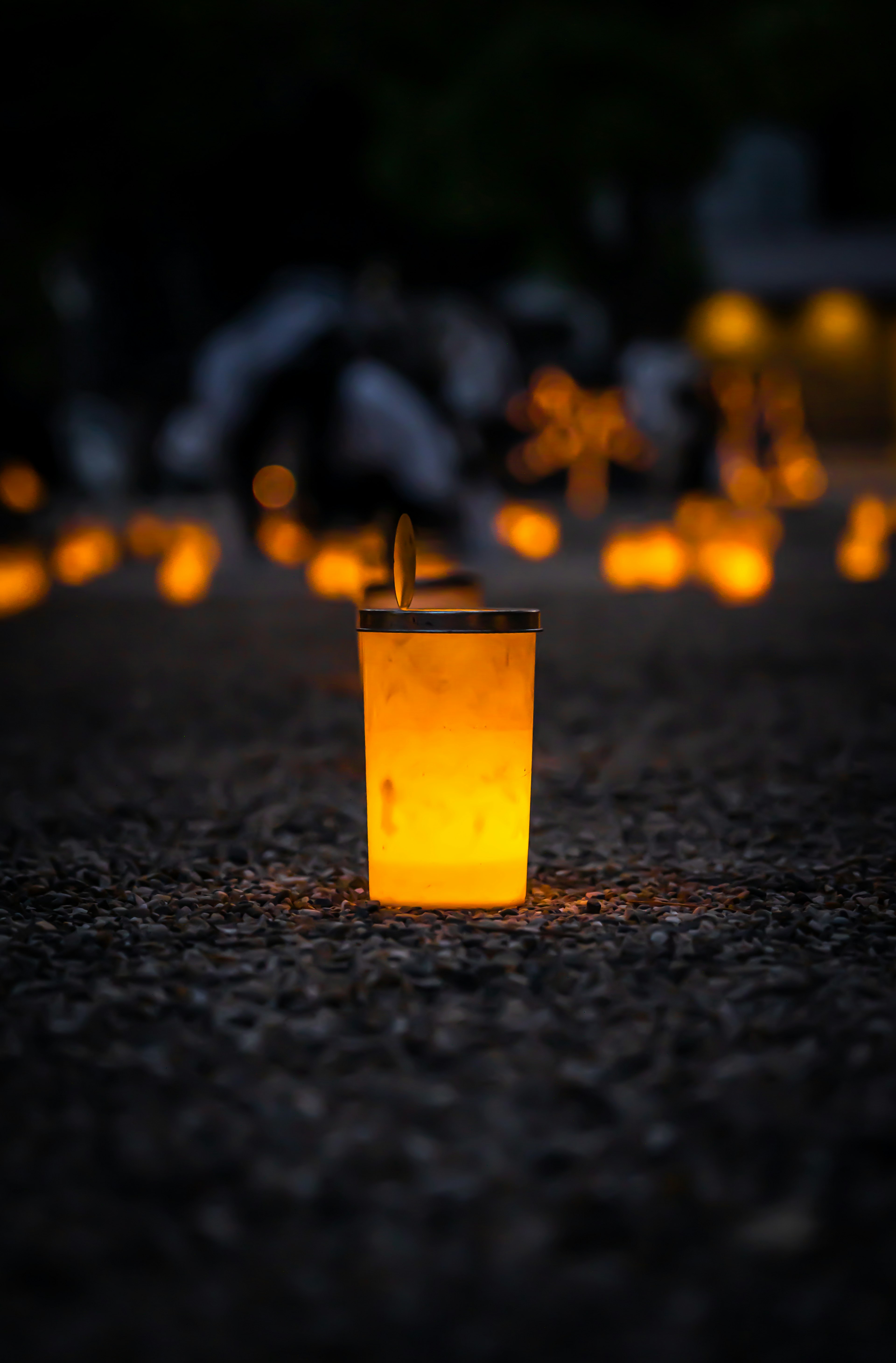 Ein transparenter Becher, der mit hellem orangefarbenem Licht leuchtet, umgeben von gedämpften Kerzenlichtern