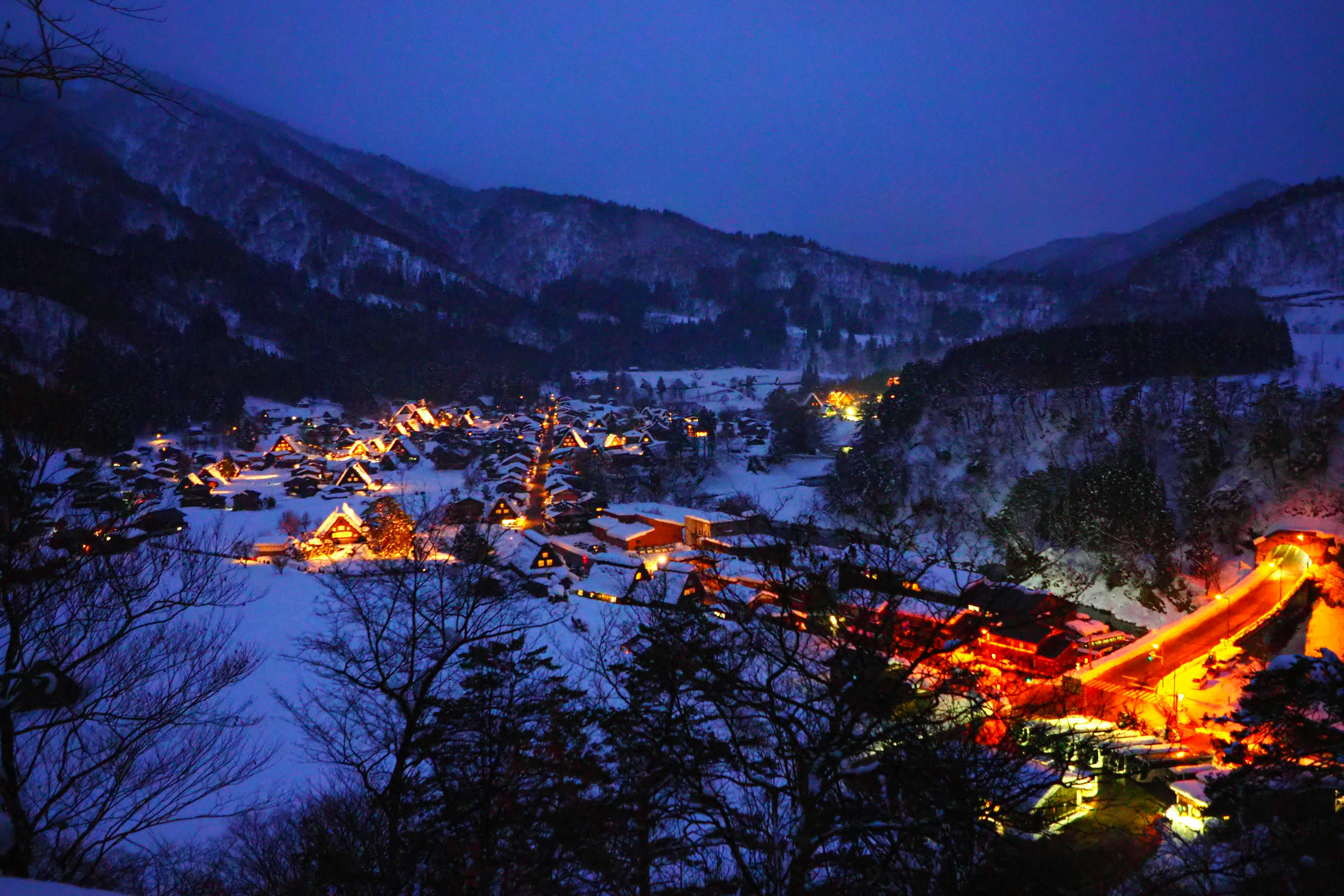 Snow-covered village at night surrounded by mountains with warm glowing houses