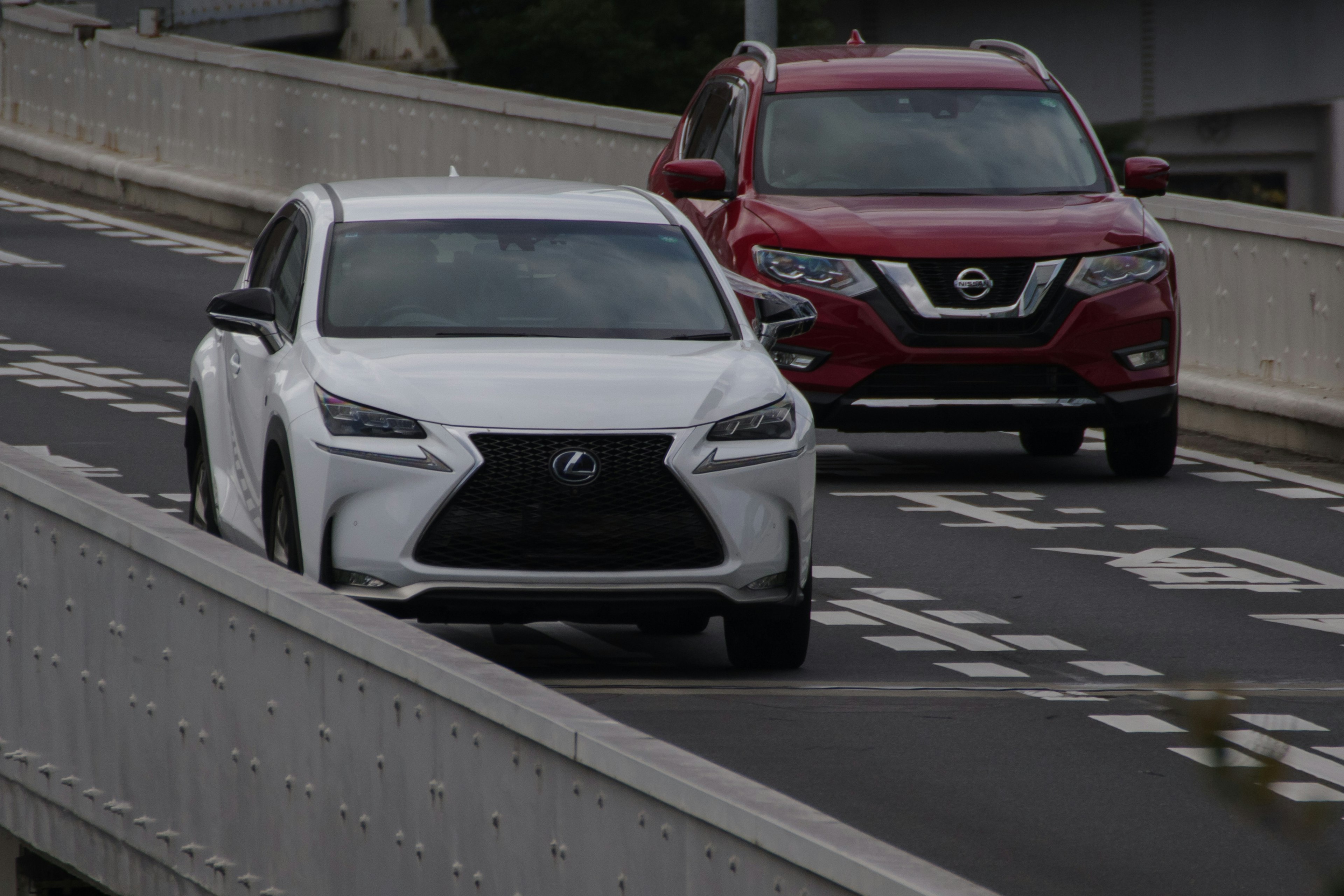 A white Lexus SUV and a red Nissan SUV driving on a highway