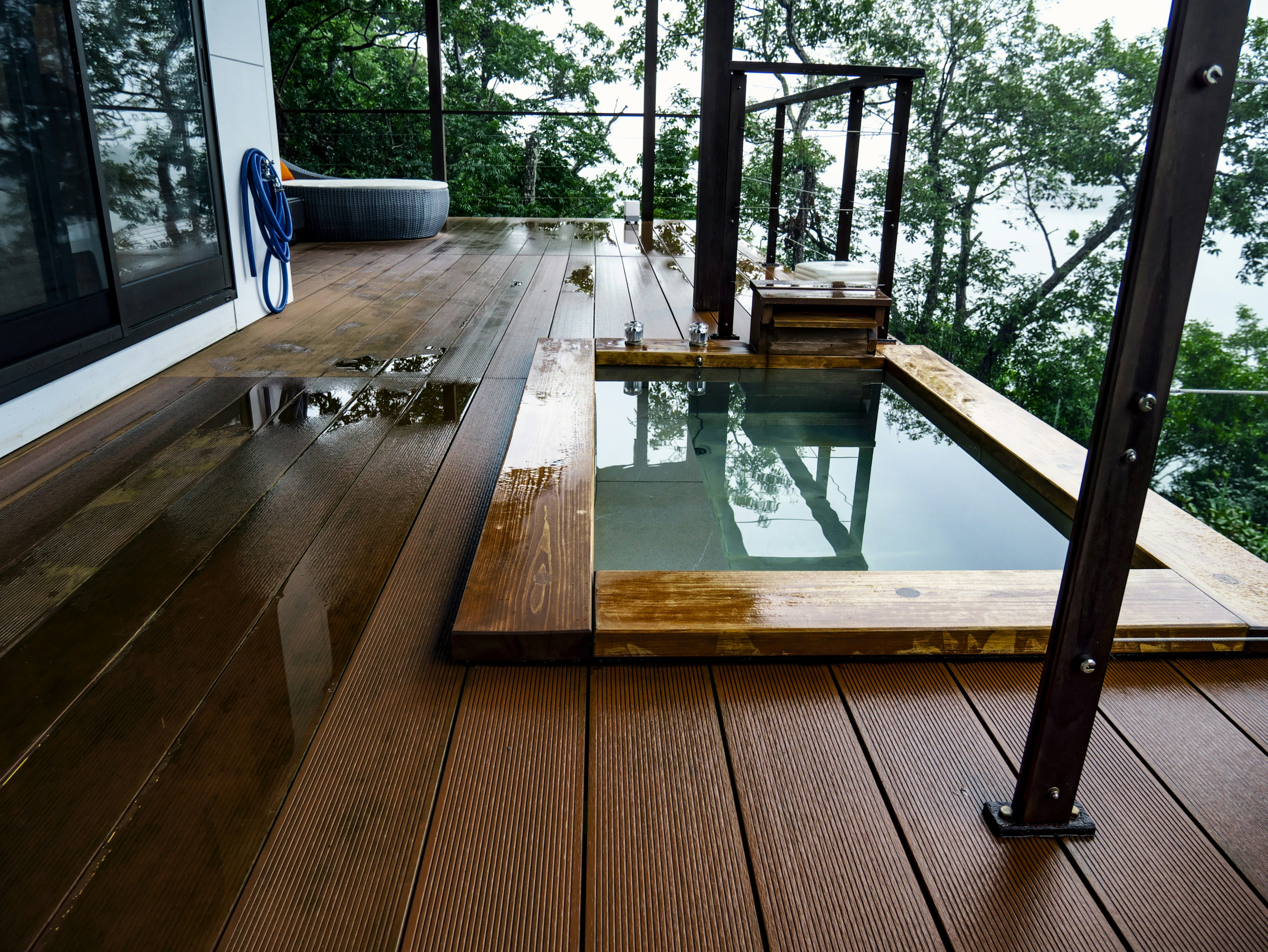 Deck de madera con una pequeña bañera y árboles al fondo