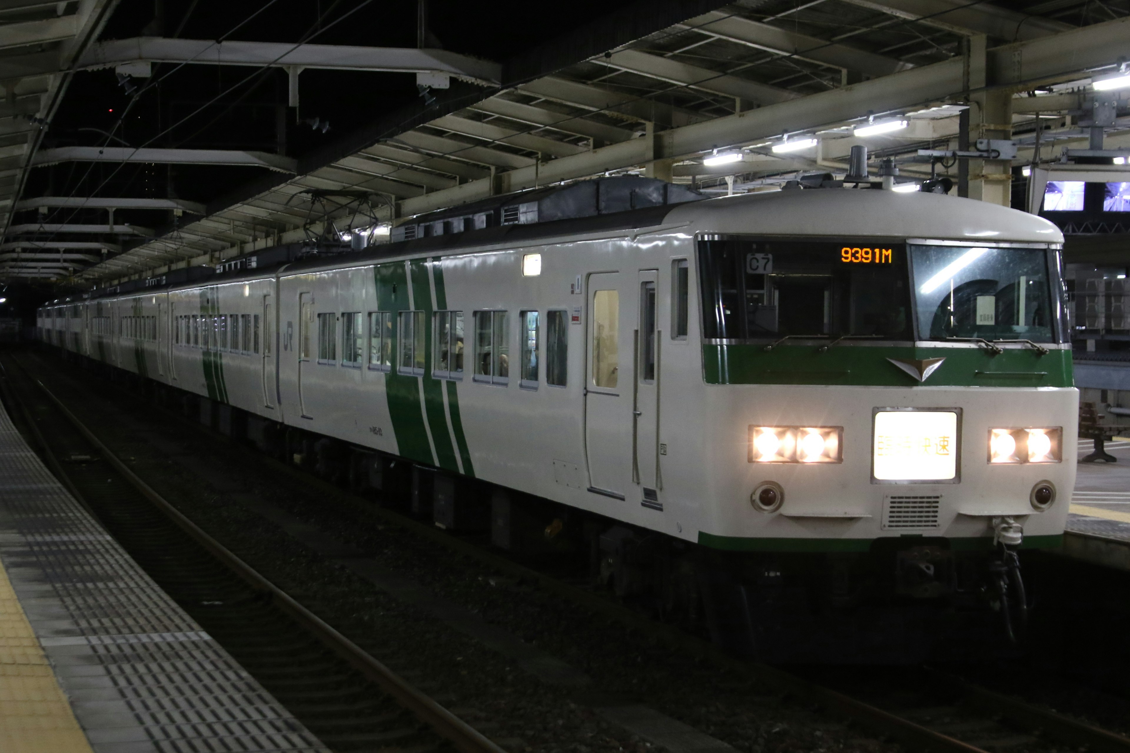 夜の駅に停車中の緑のストライプのある白い列車