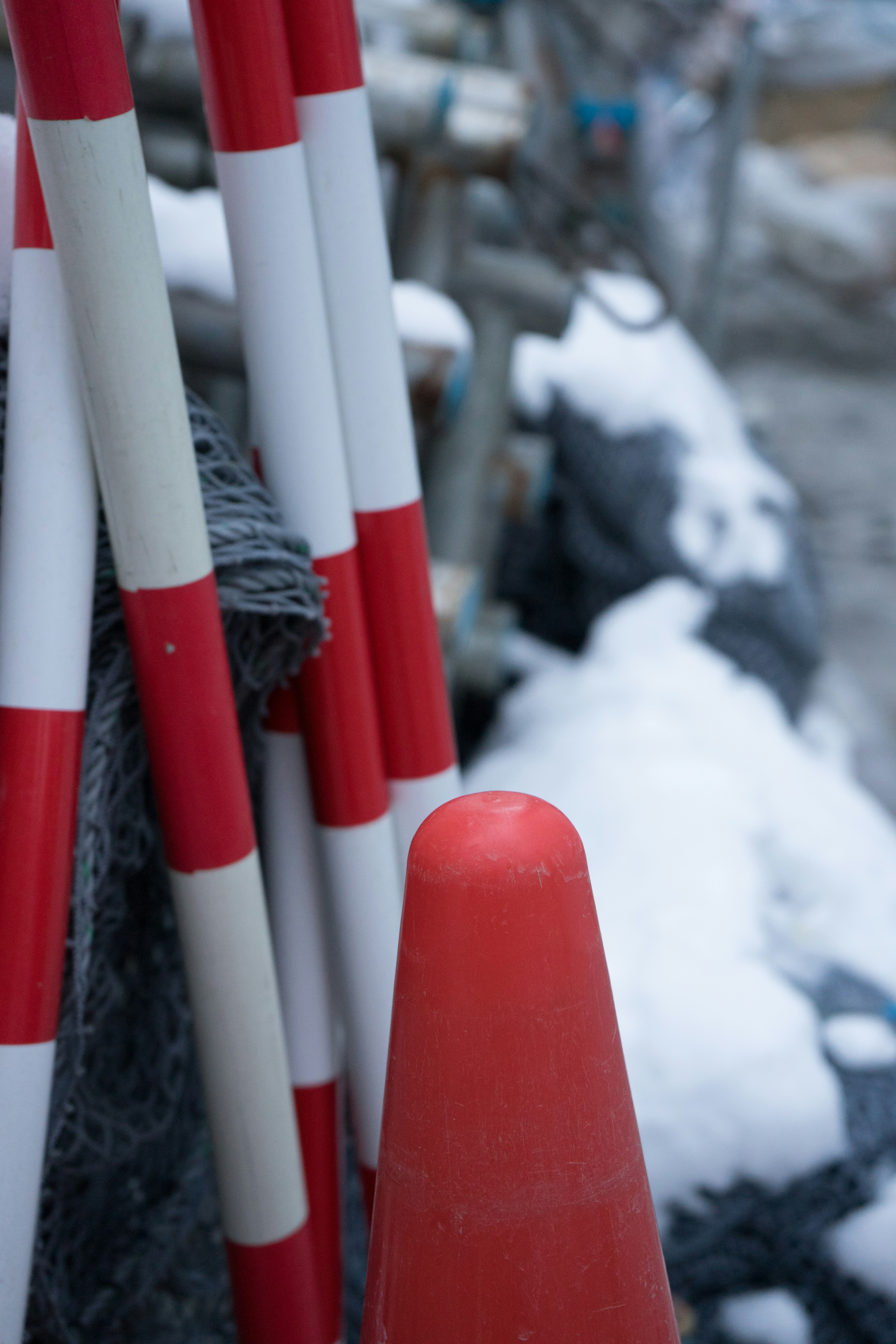 Red and white construction markers and cone covered in snow