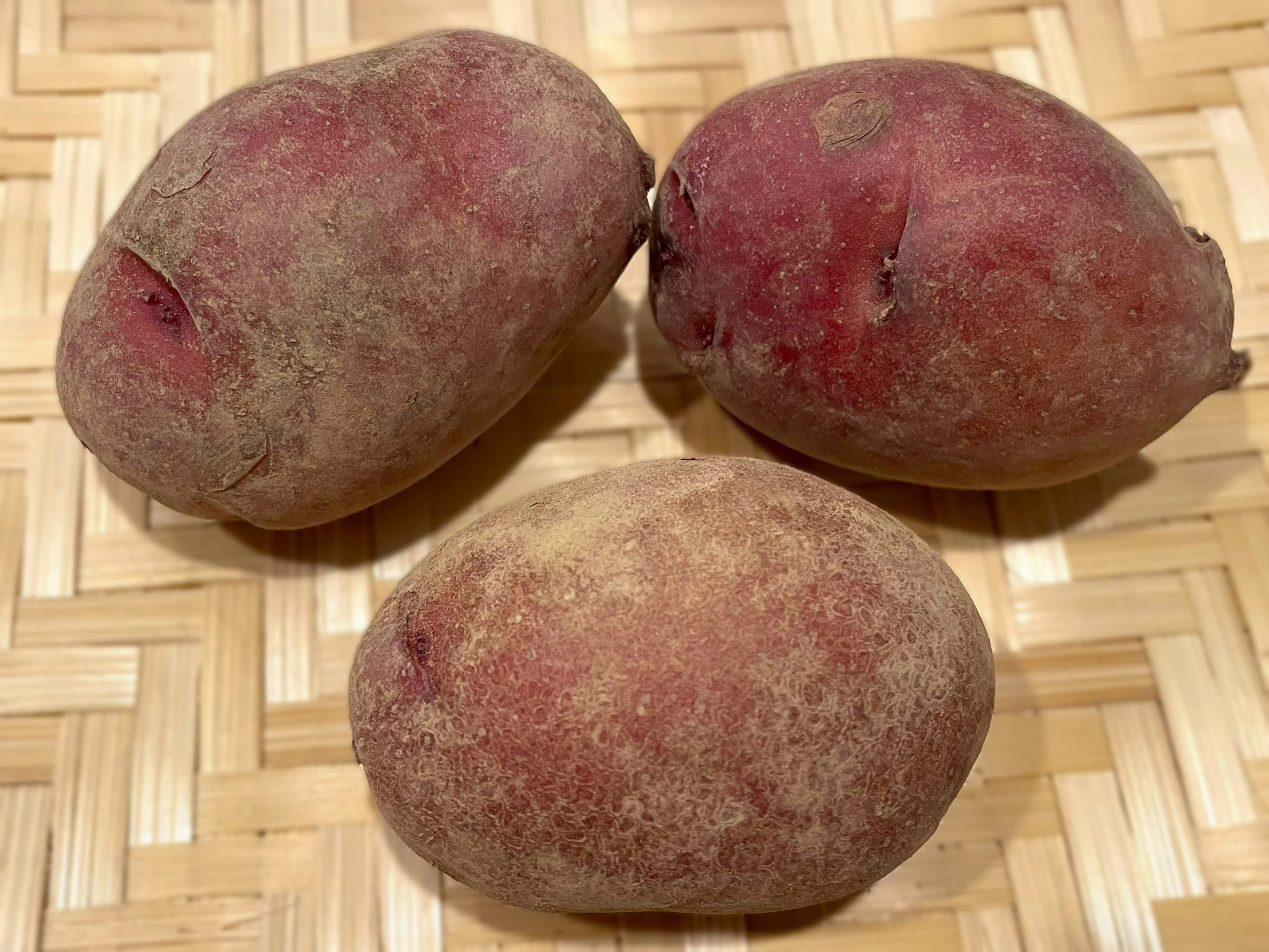 Three red-skinned potatoes on a bamboo mat