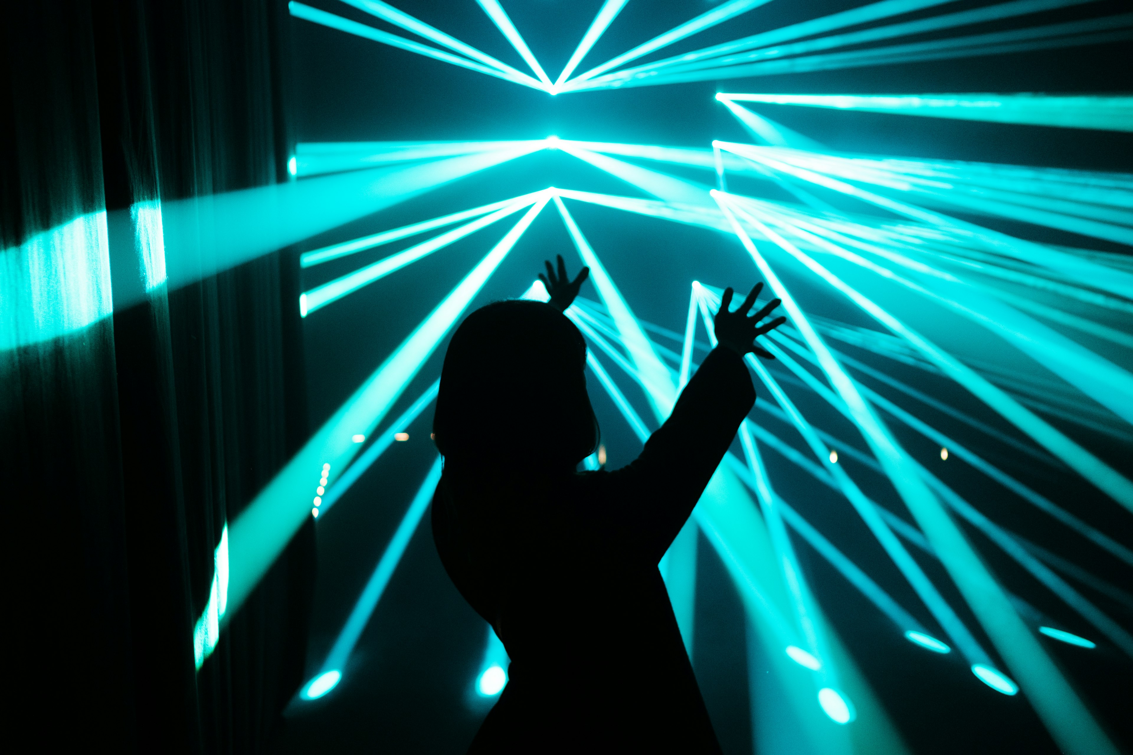 Silhouette of a person raising hands amidst blue laser lights