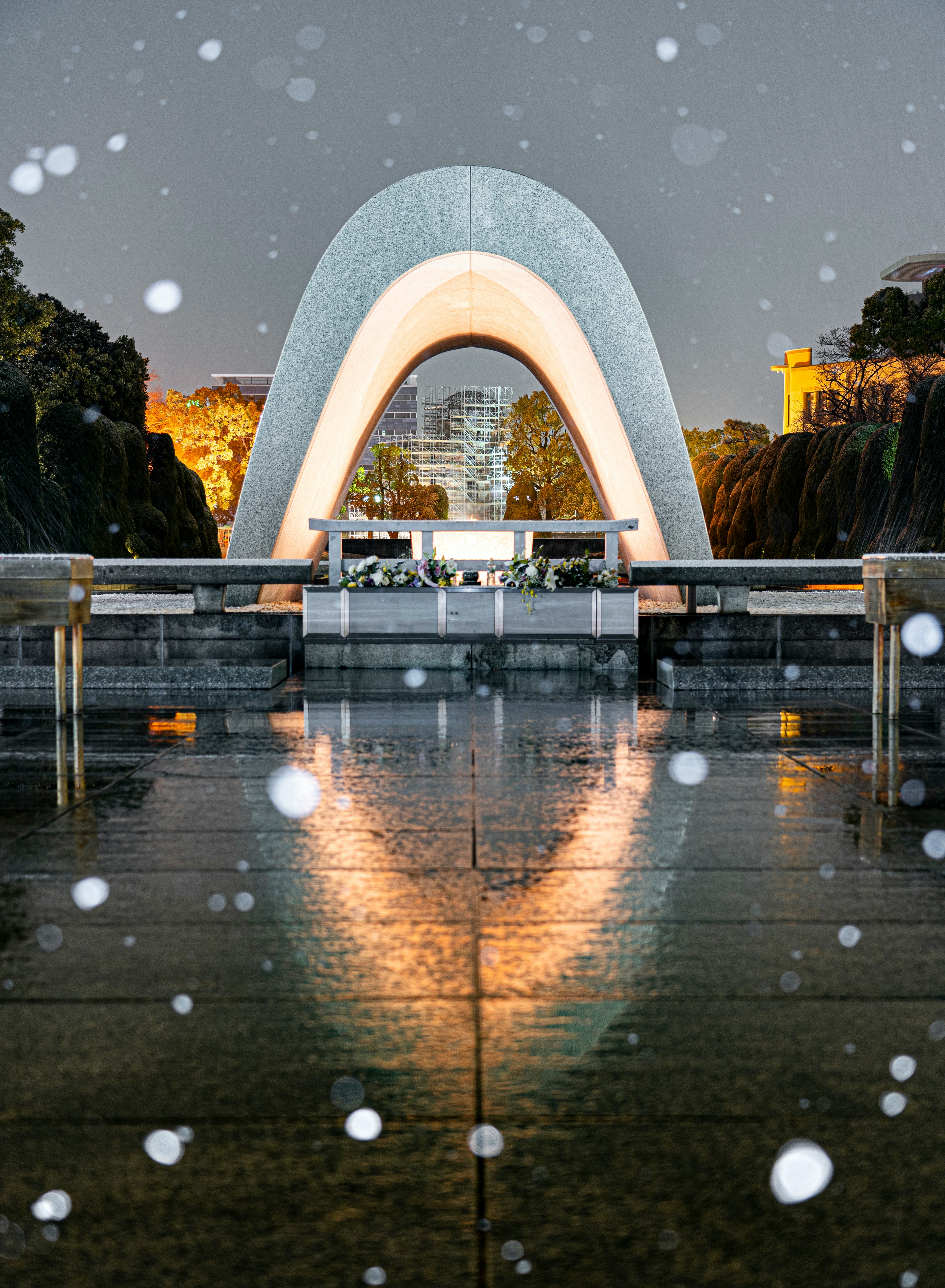 Beleuchtetes weißes Bogenmonument im Schnee bei Nacht mit Reflexionen auf dem Wasser