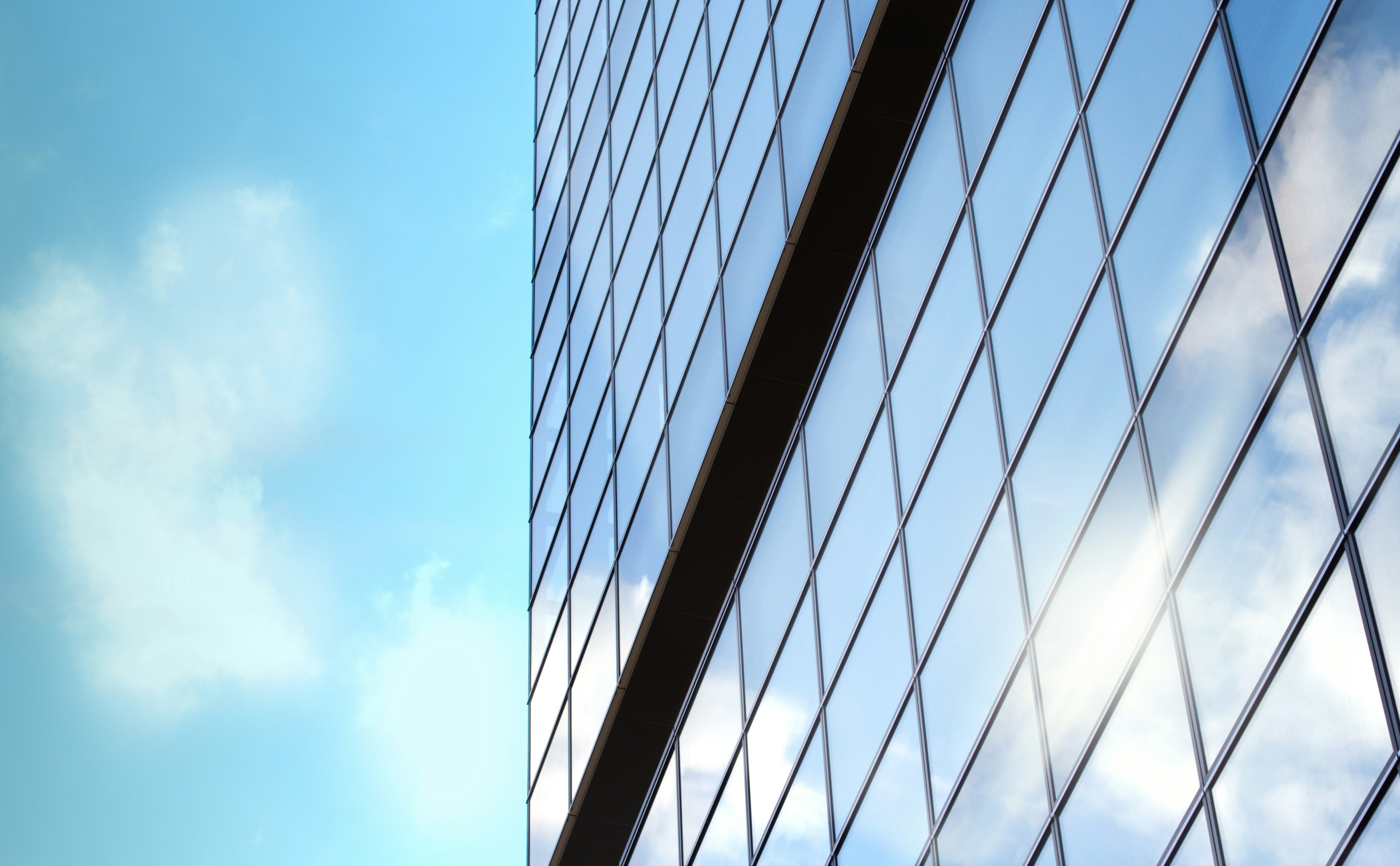 Part of a glass building reflecting blue sky and clouds