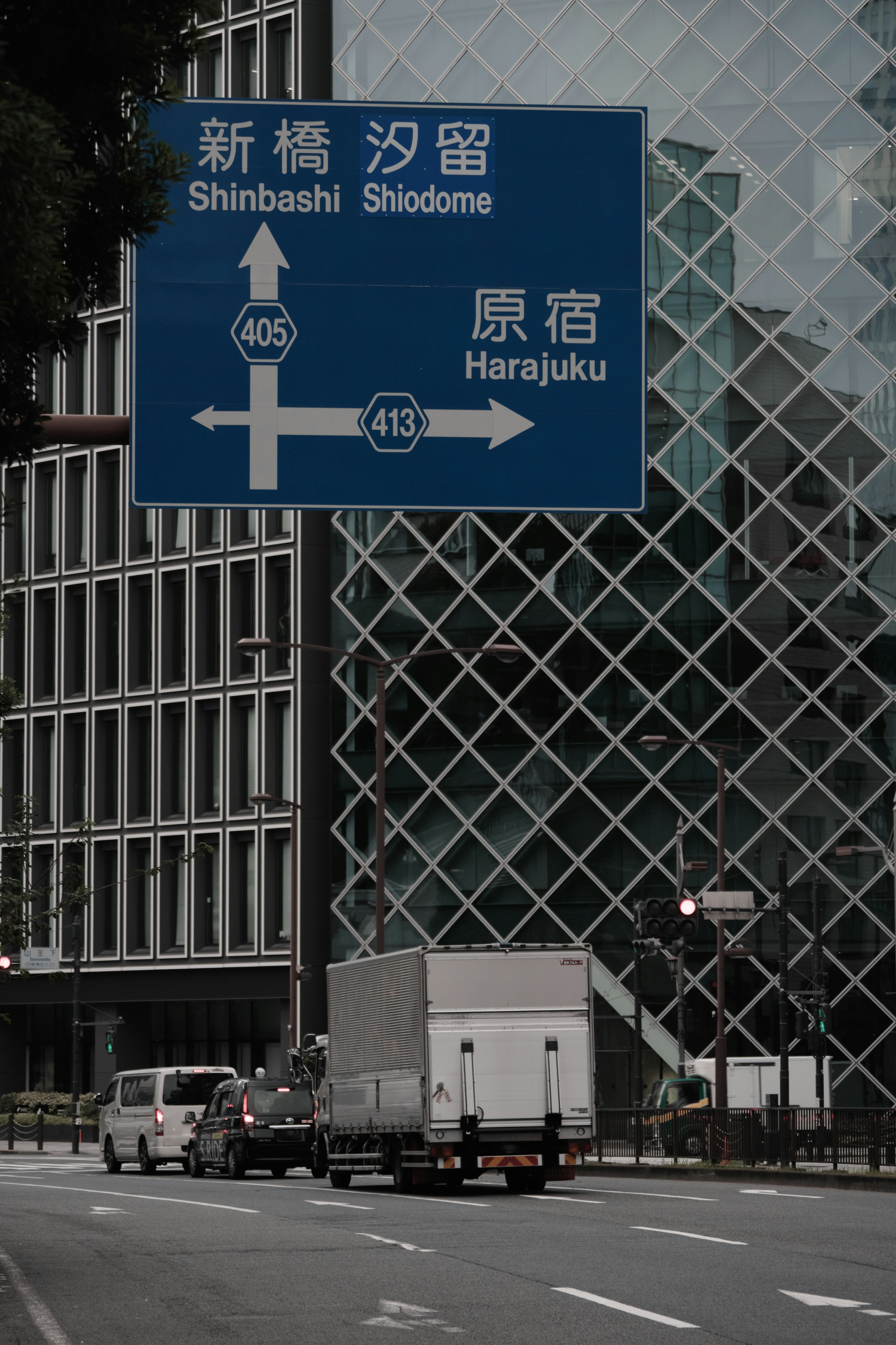 Blaues Verkehrsschild, das Shinbashi und Harajuku anzeigt, mit modernen Gebäuden im Hintergrund