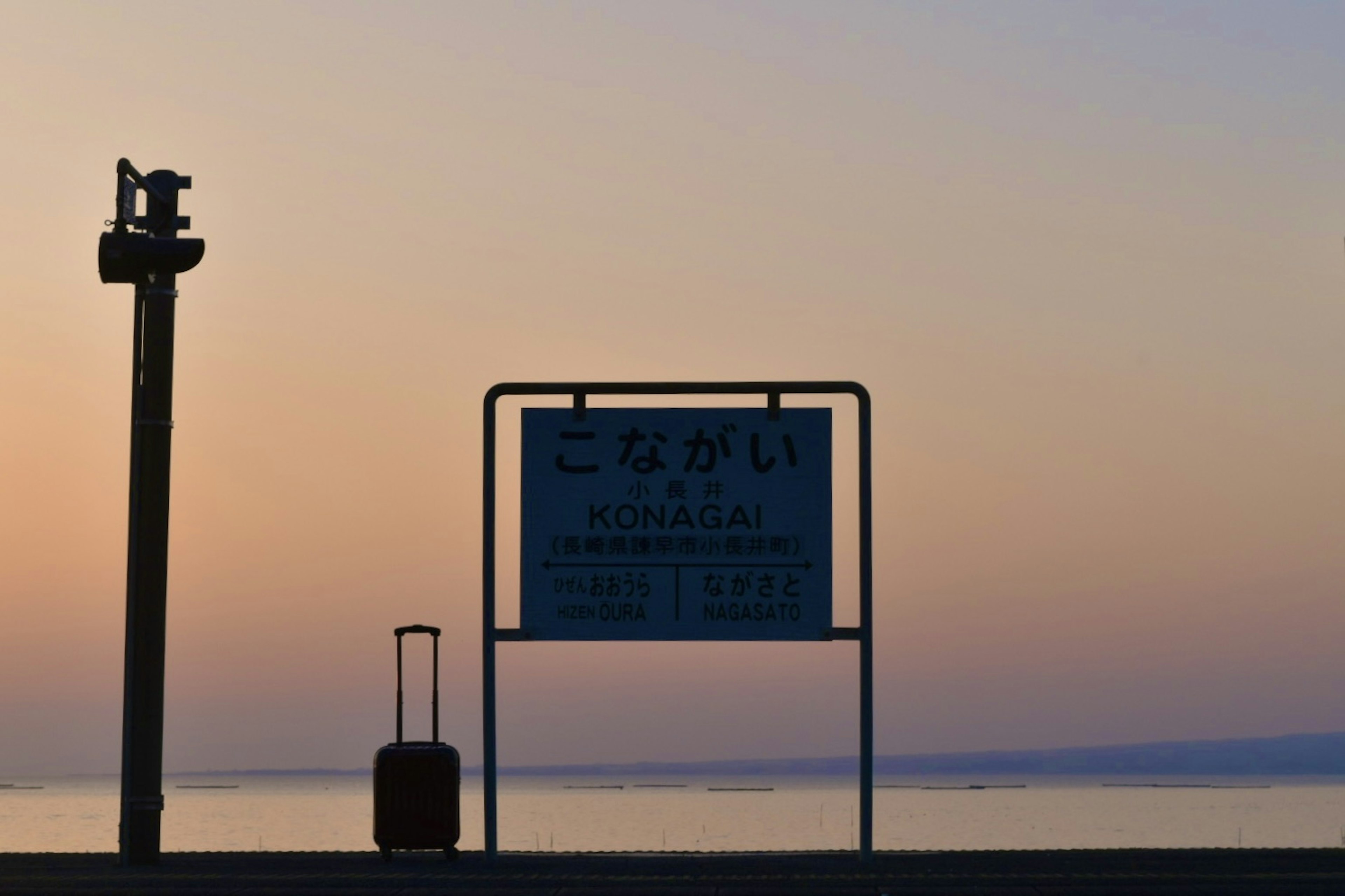 夕焼けの海岸に立つ看板と荷物