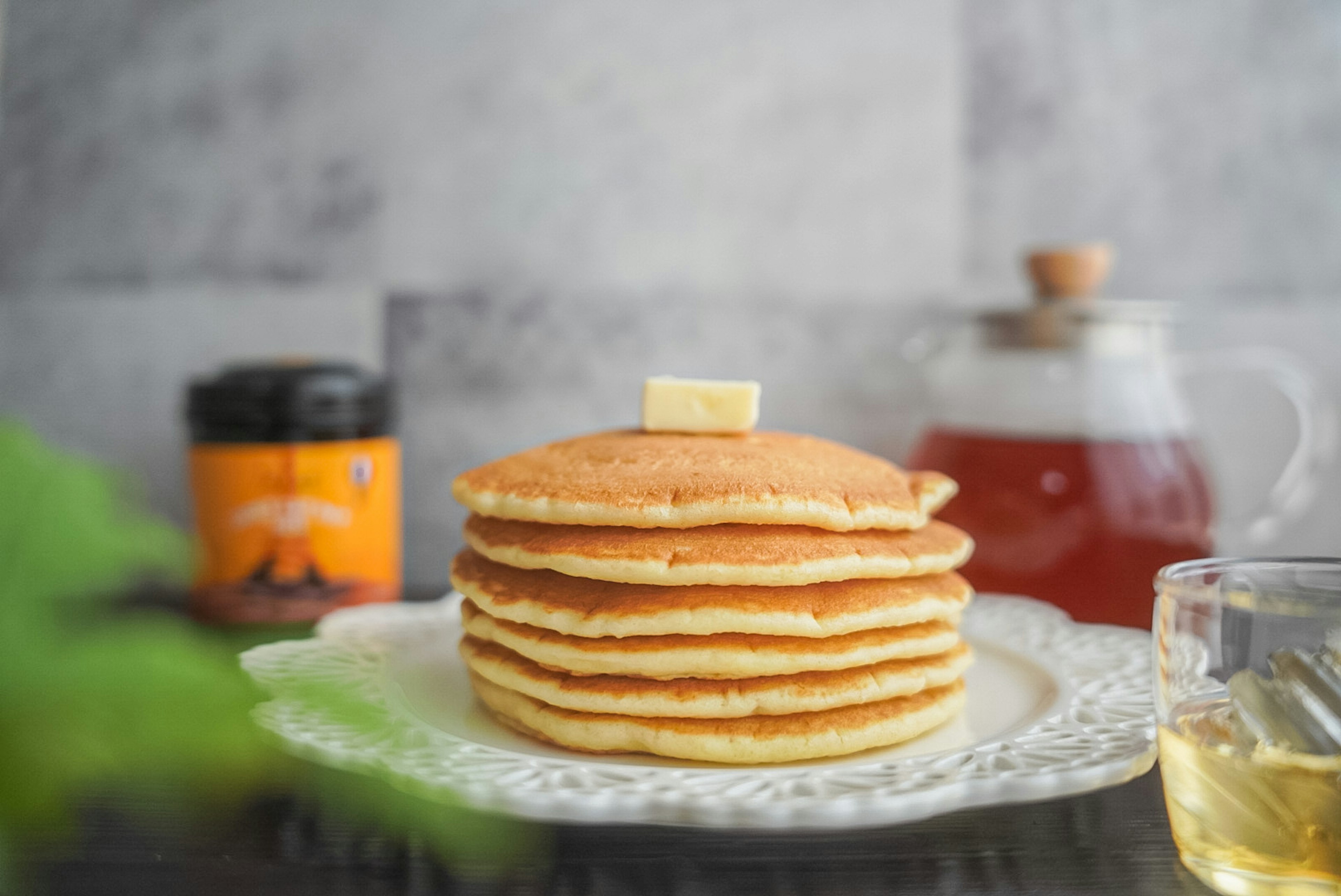 Tumpukan pancake dengan mentega di atas piring dekoratif dengan teh dan stoples madu di latar belakang