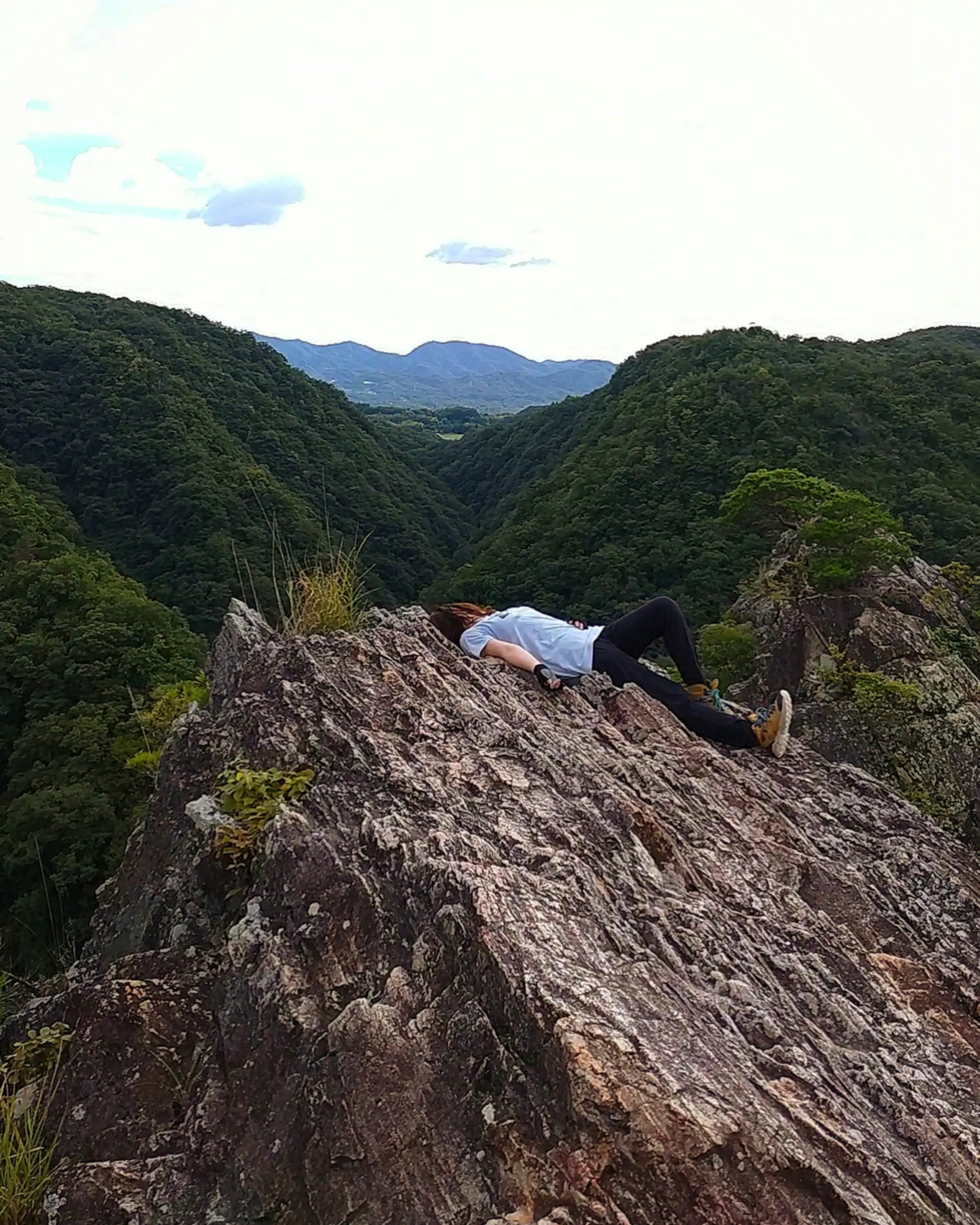 Person lying on a rocky ledge with lush green mountains in the background