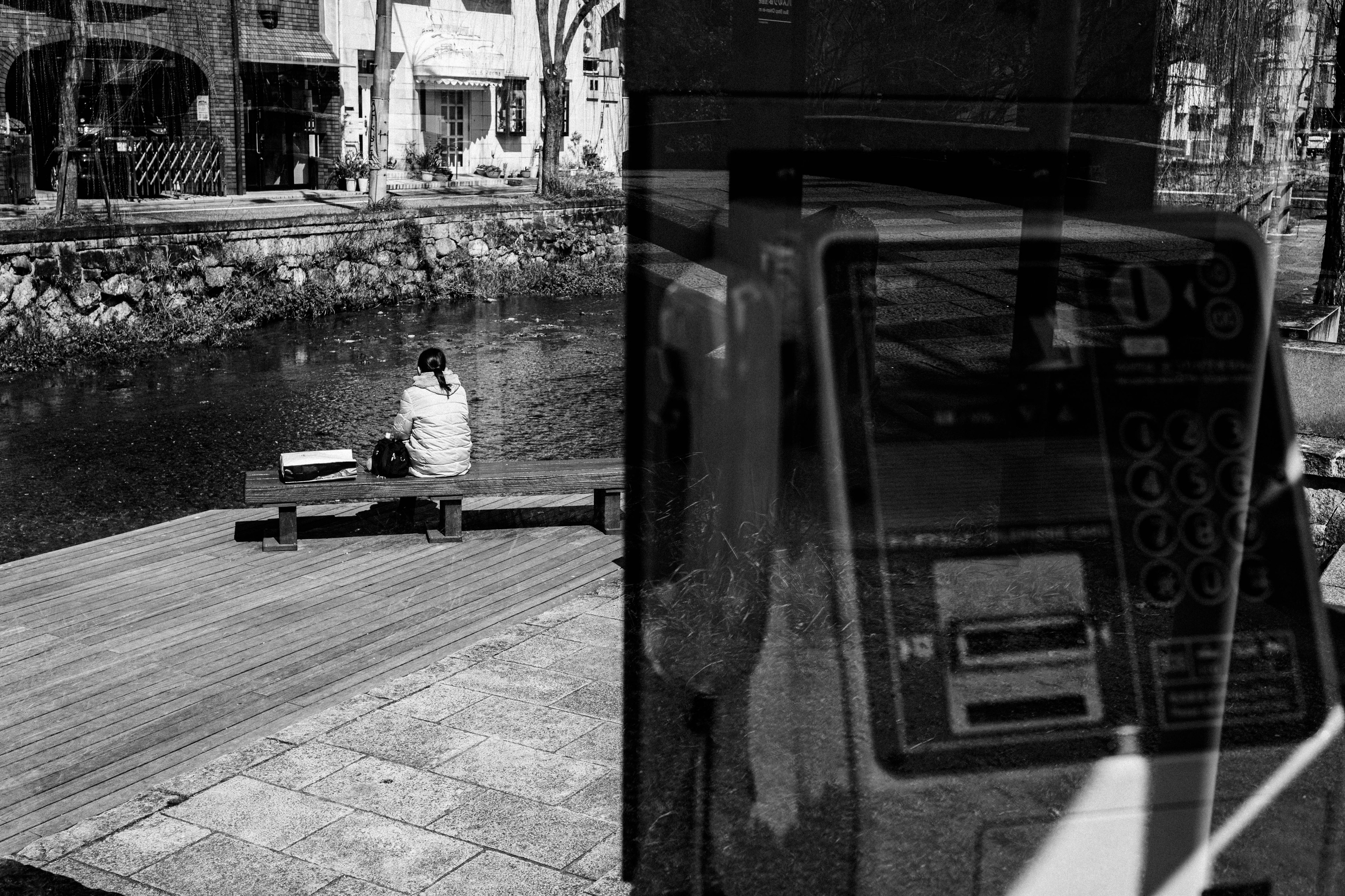 川辺に座る女性と背景の街並みを映したモノクロ写真