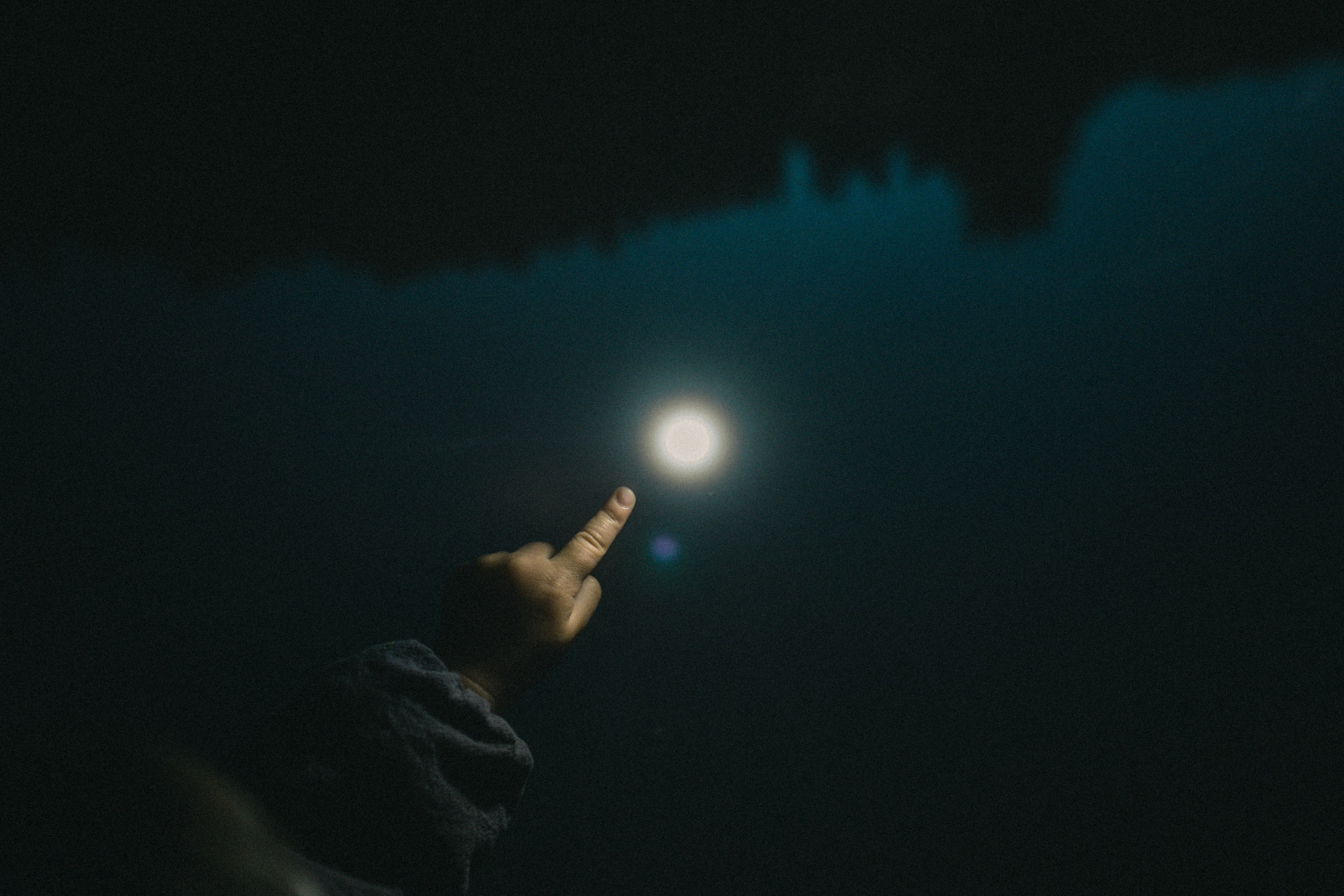 Silhouette di una mano che si estende verso la luce della luna riflessa su una superficie scura