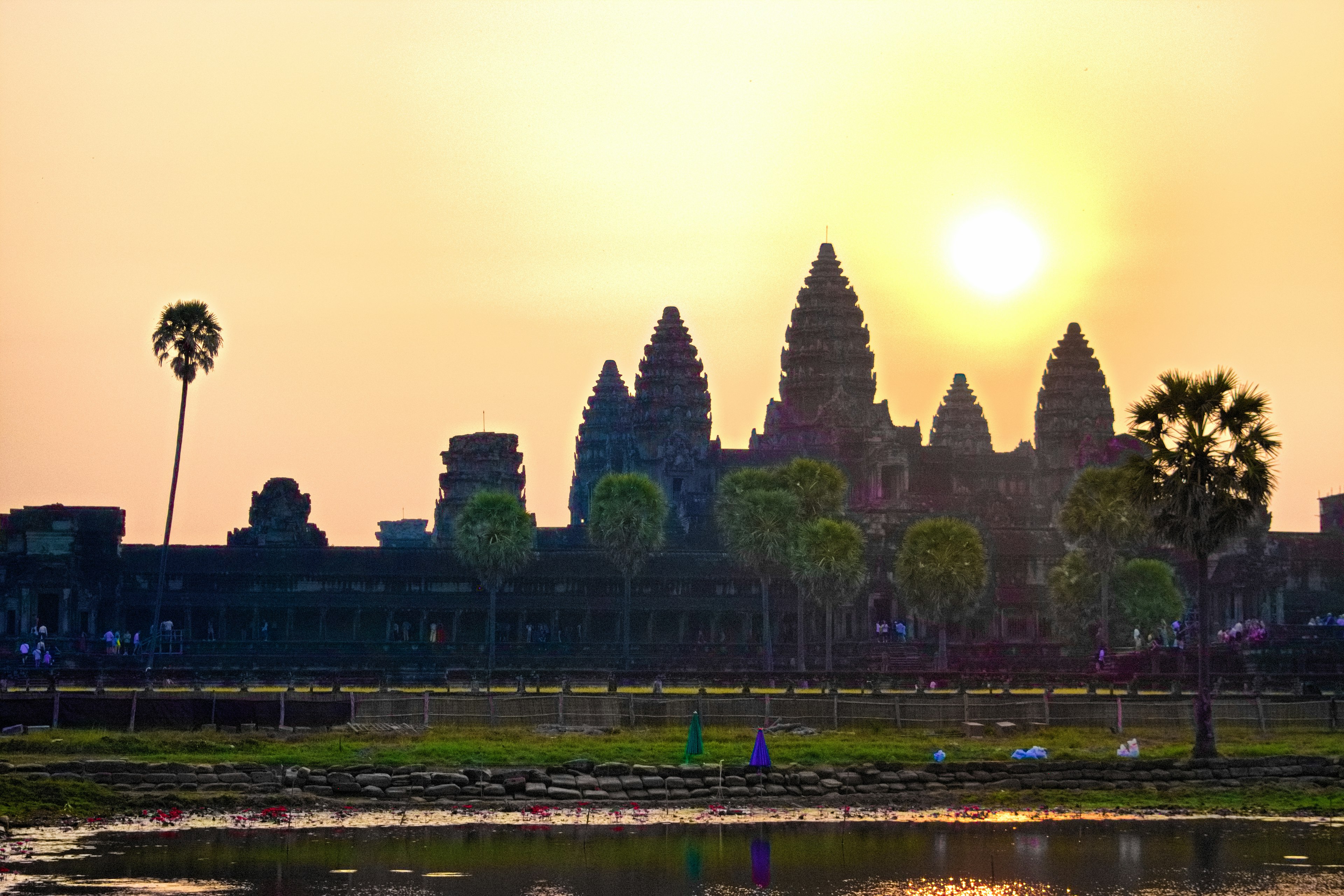 Silhouette of Angkor Wat against the sunset with palm trees and water