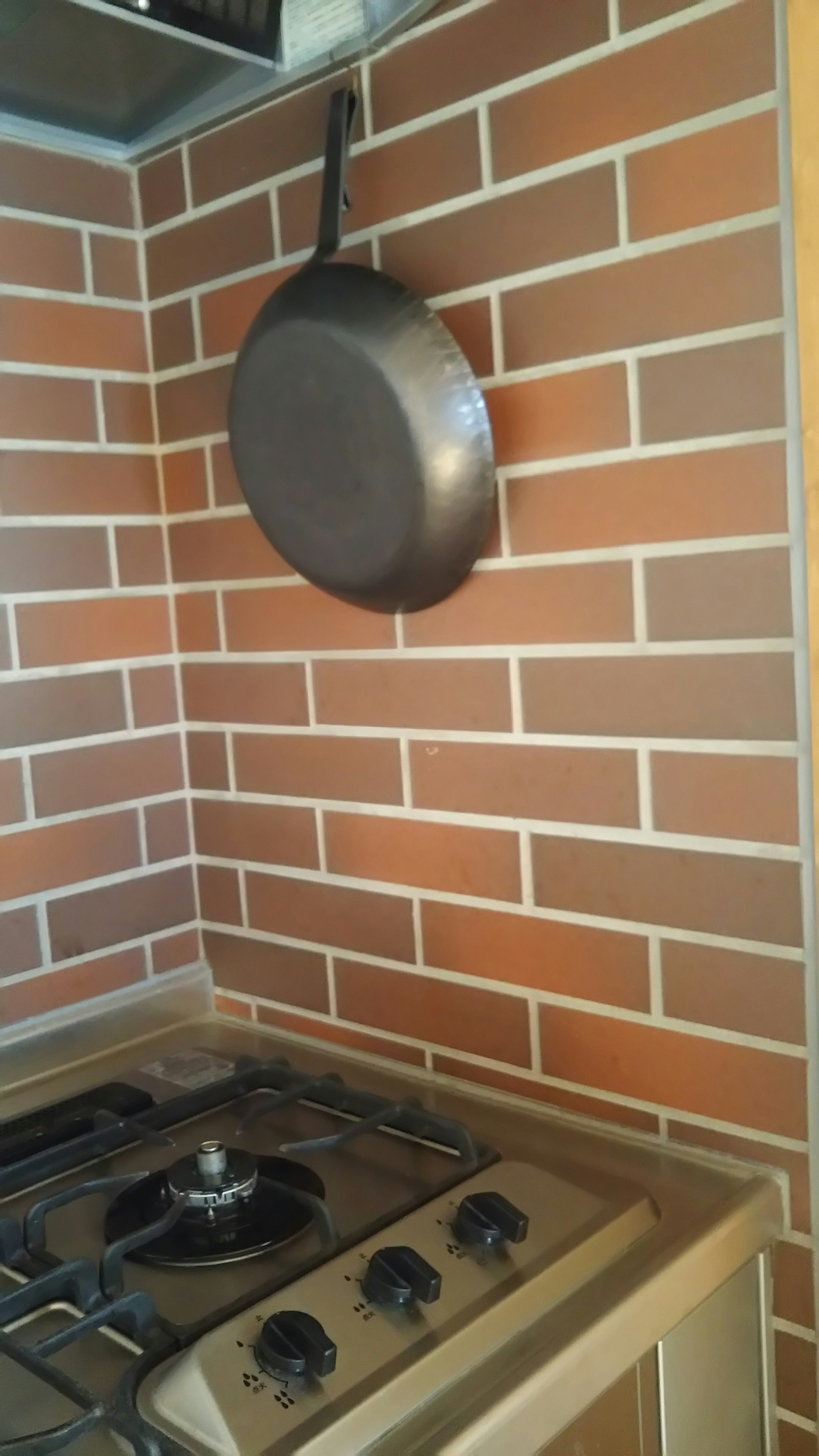 Esquina de cocina con una sartén colgada en una pared de azulejos marrones y una estufa de gas