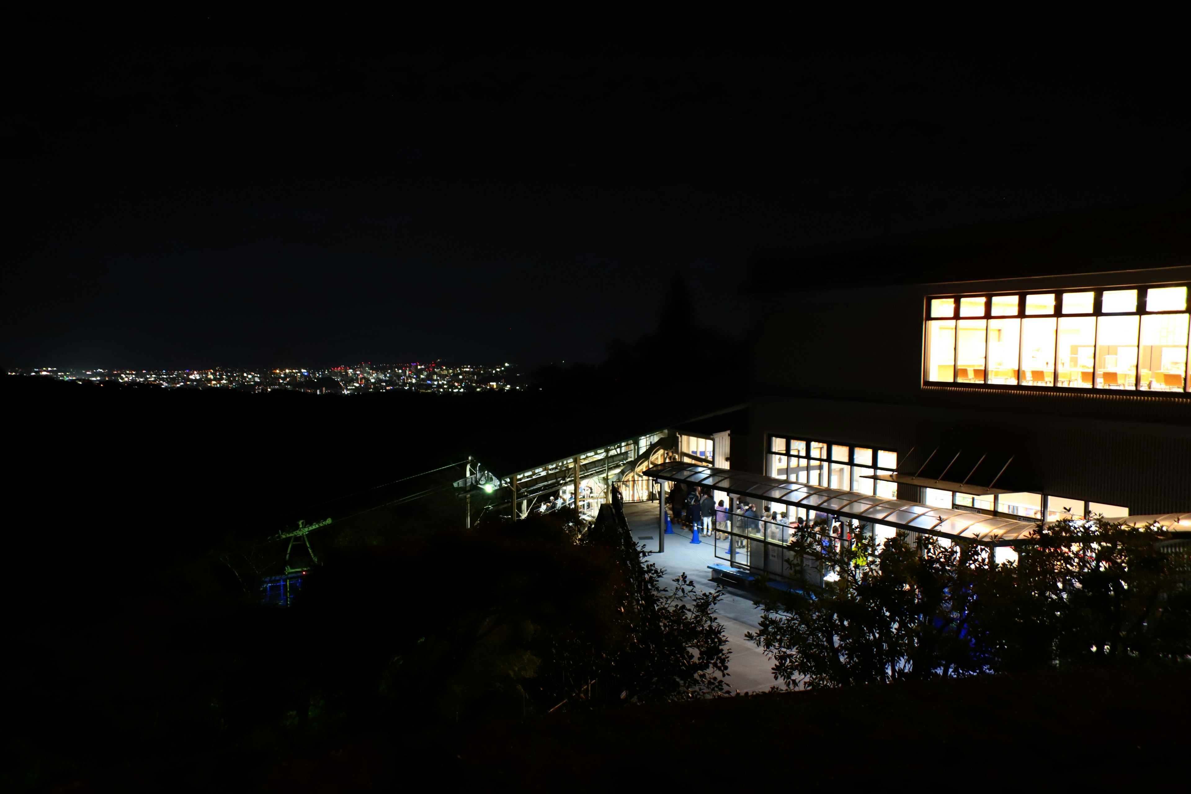 Edificio iluminado por la noche rodeado de naturaleza y luces de la ciudad a lo lejos