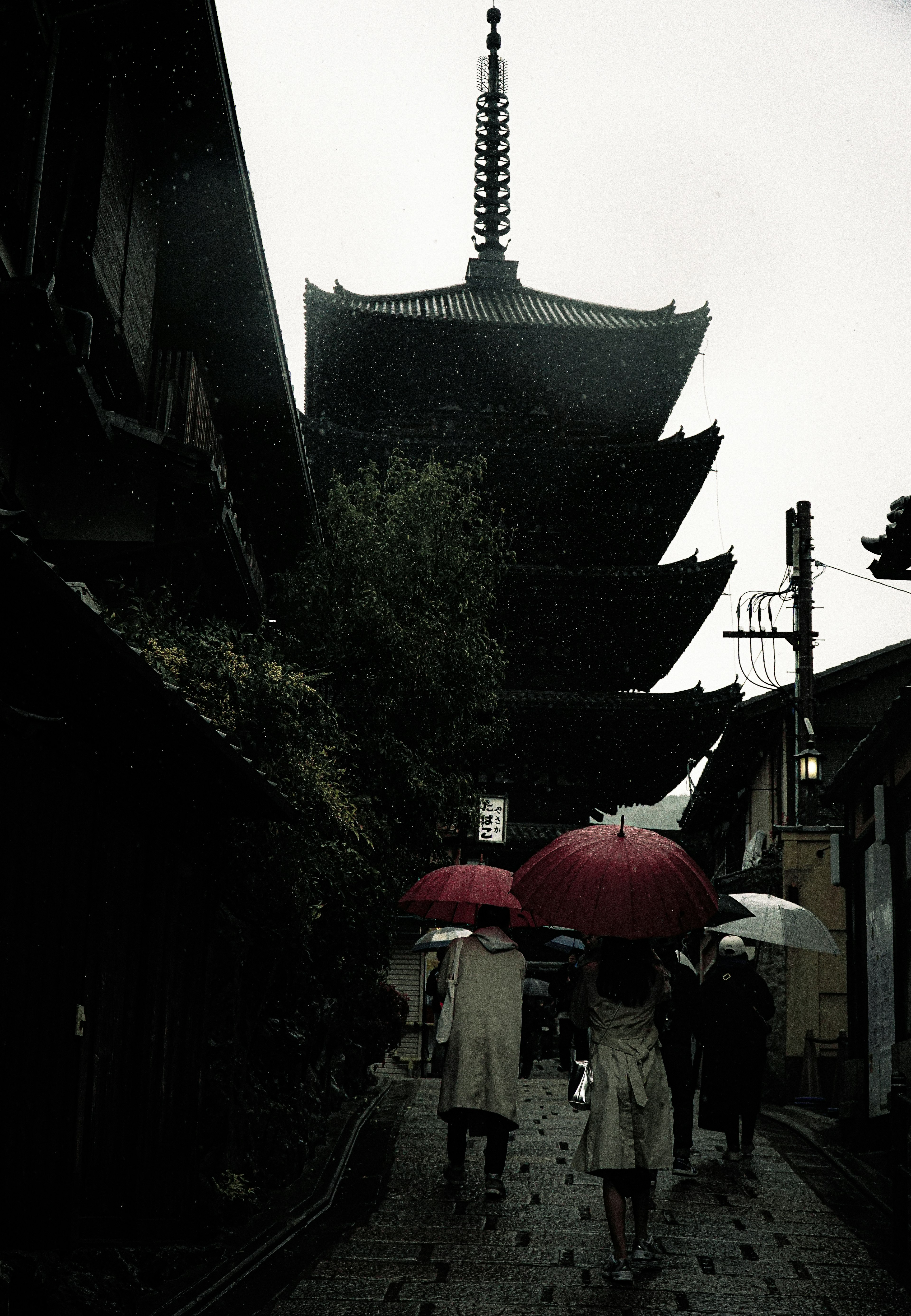 Silhouette einer Pagode mit Menschen, die bei Regen unter Regenschirmen gehen