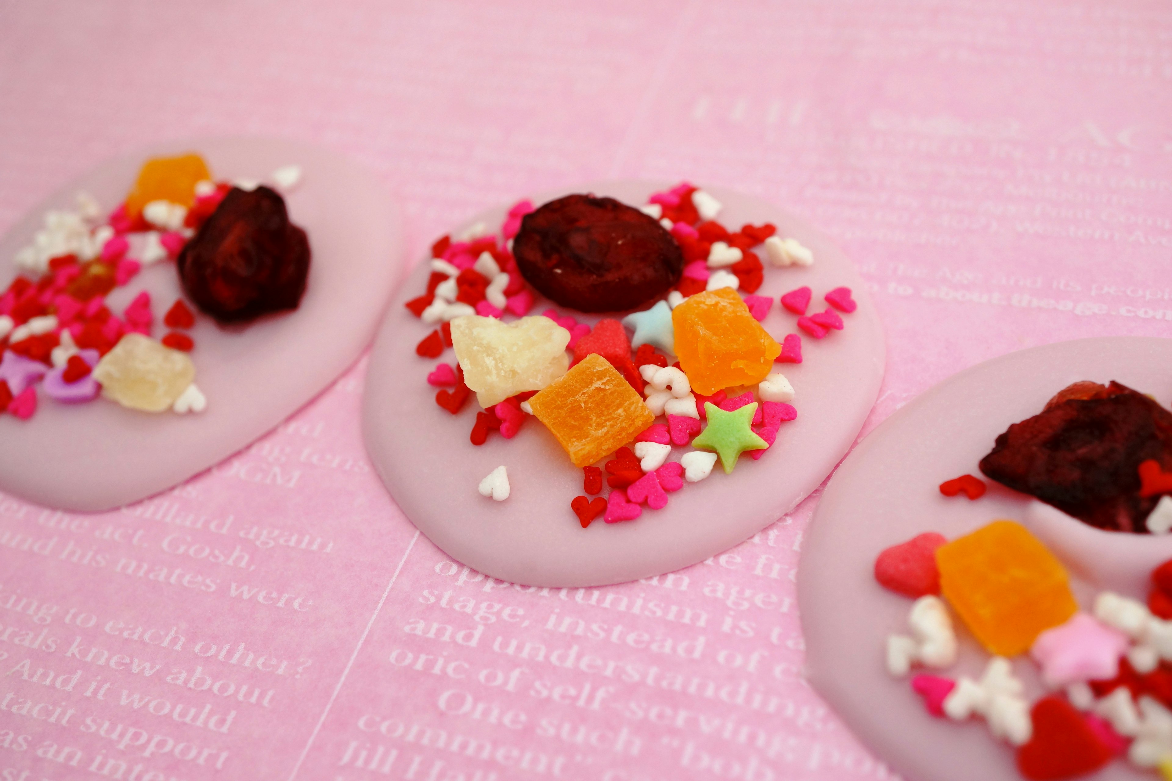 White candy topped with colorful sprinkles on a pink background