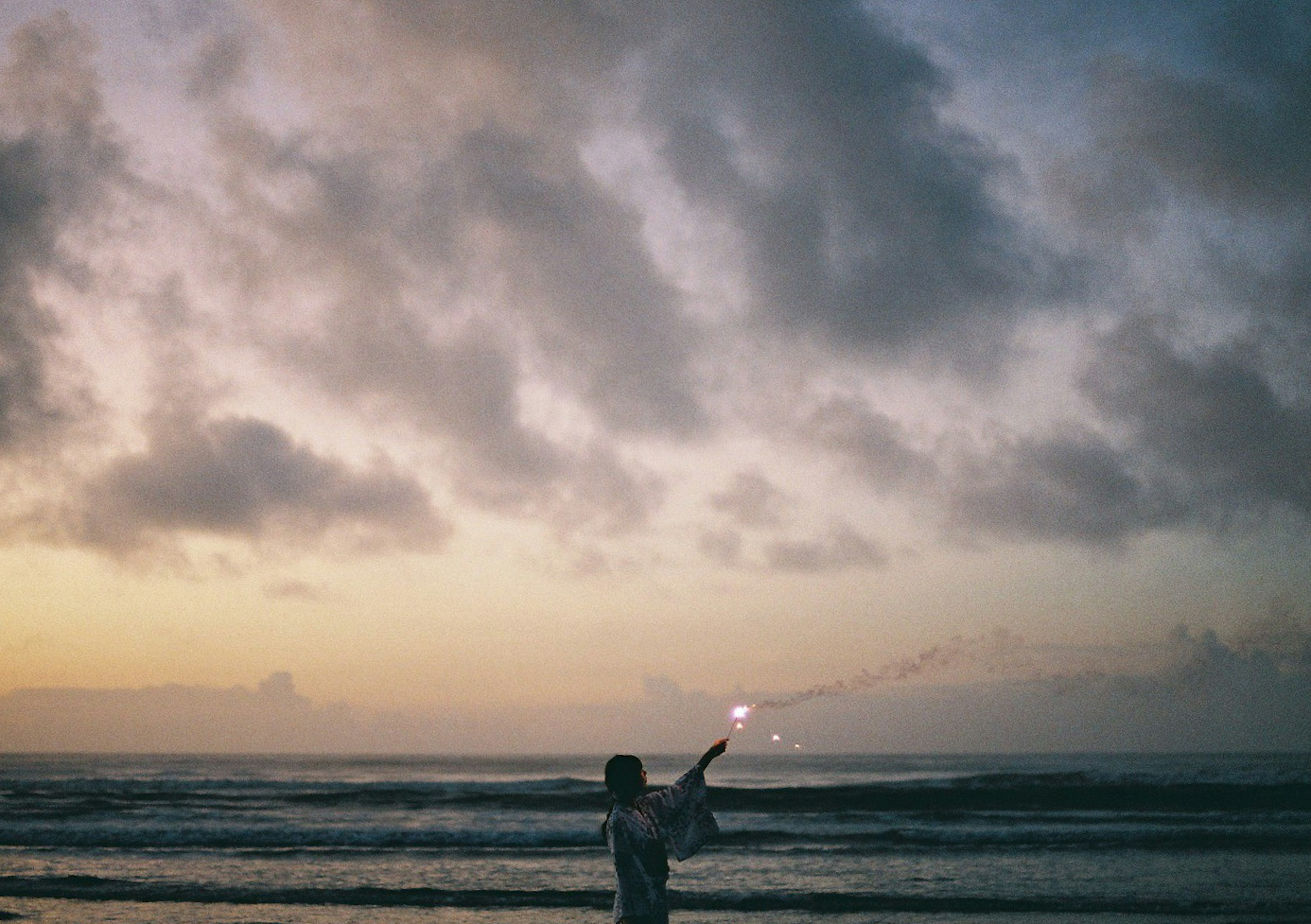 Silhouette seseorang memegang kembang api di pantai saat matahari terbenam