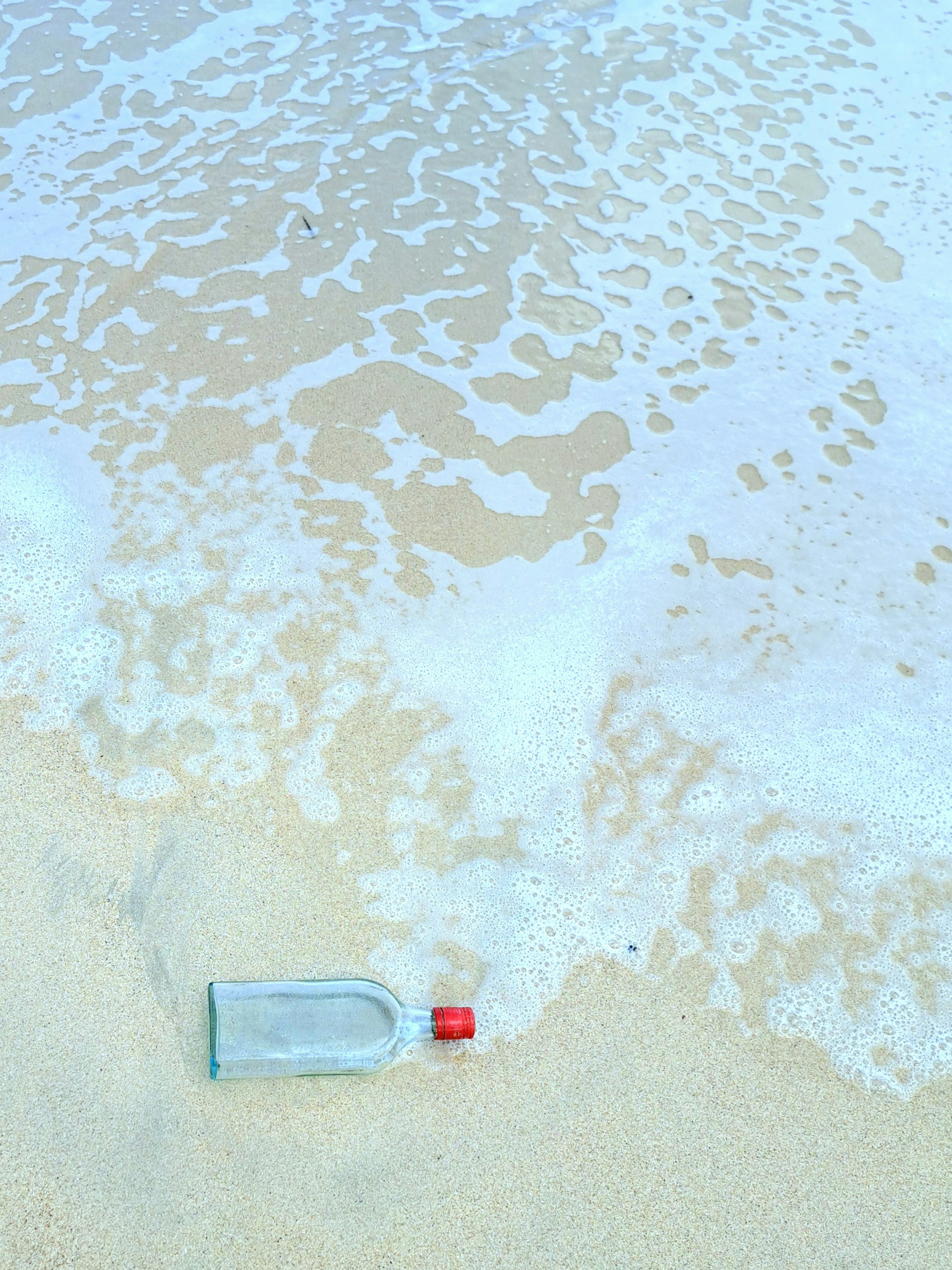 Una botella clara con tapa roja arrastrada por las olas en la playa